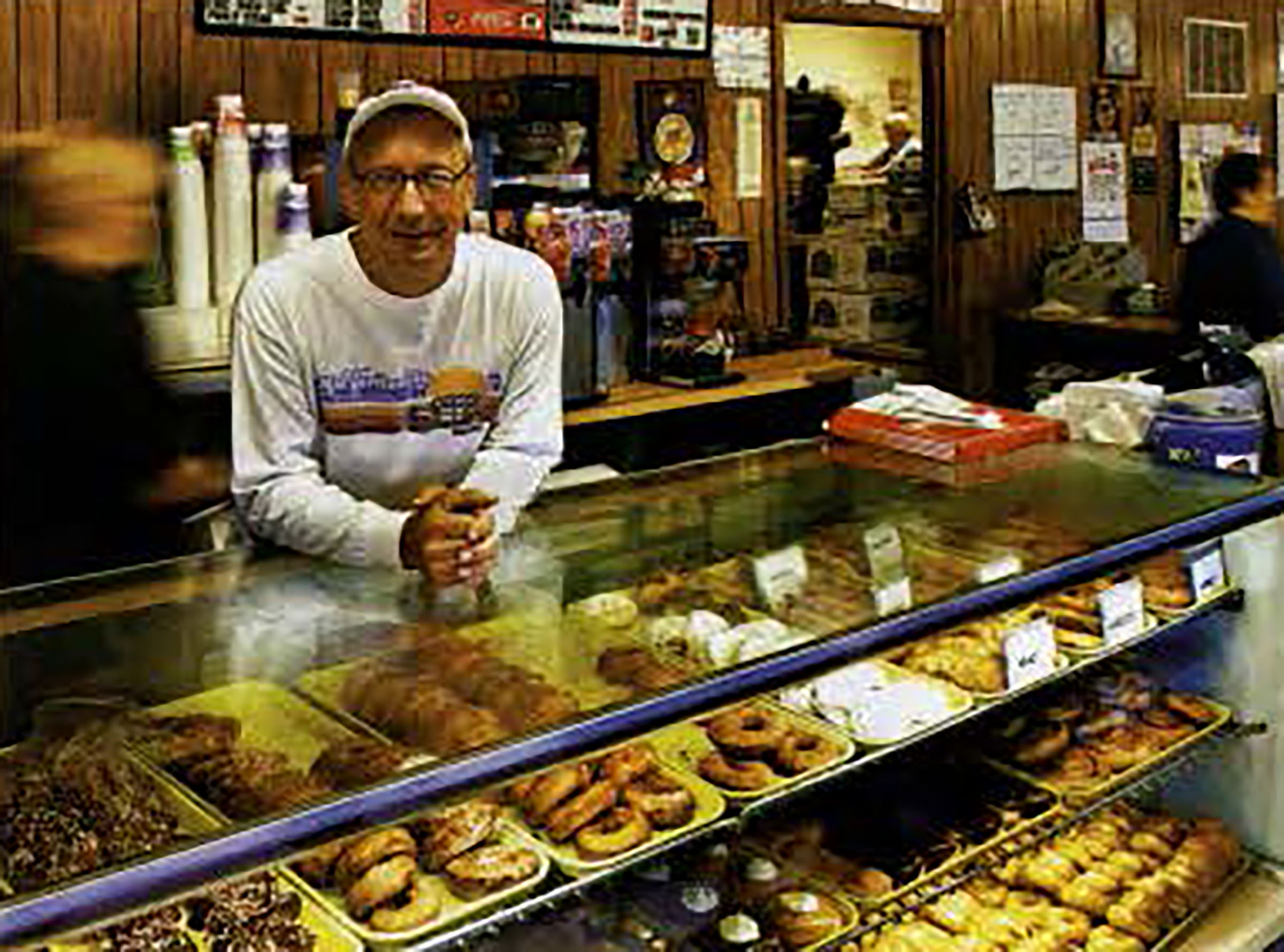 Photo of restaurant's owner leaning on top case of donuts