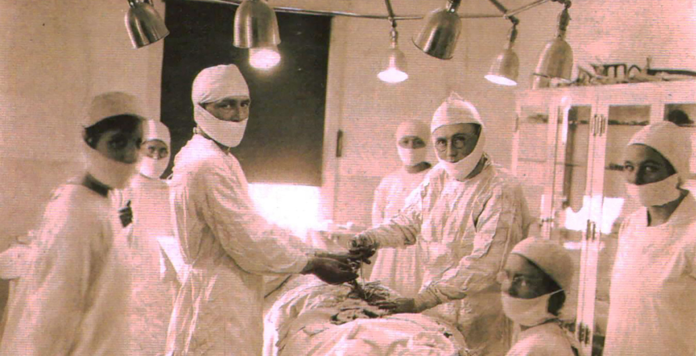 Seven people standing around a surgical table performing on a patient