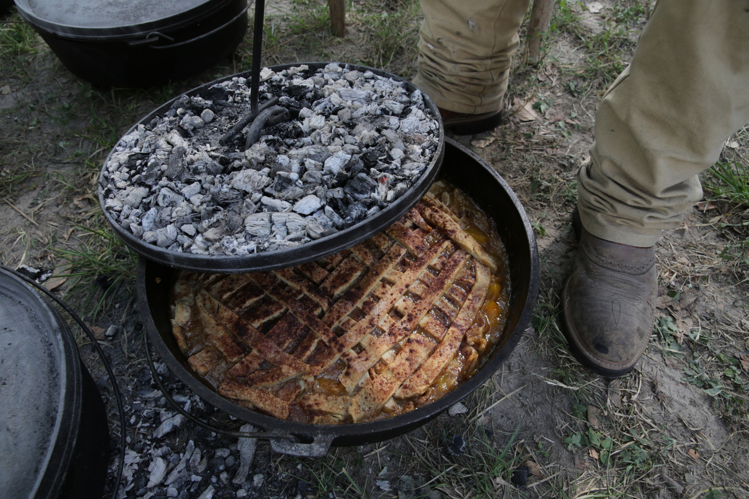 Coals on top of the lid of a dark cast iron oven containing a pie