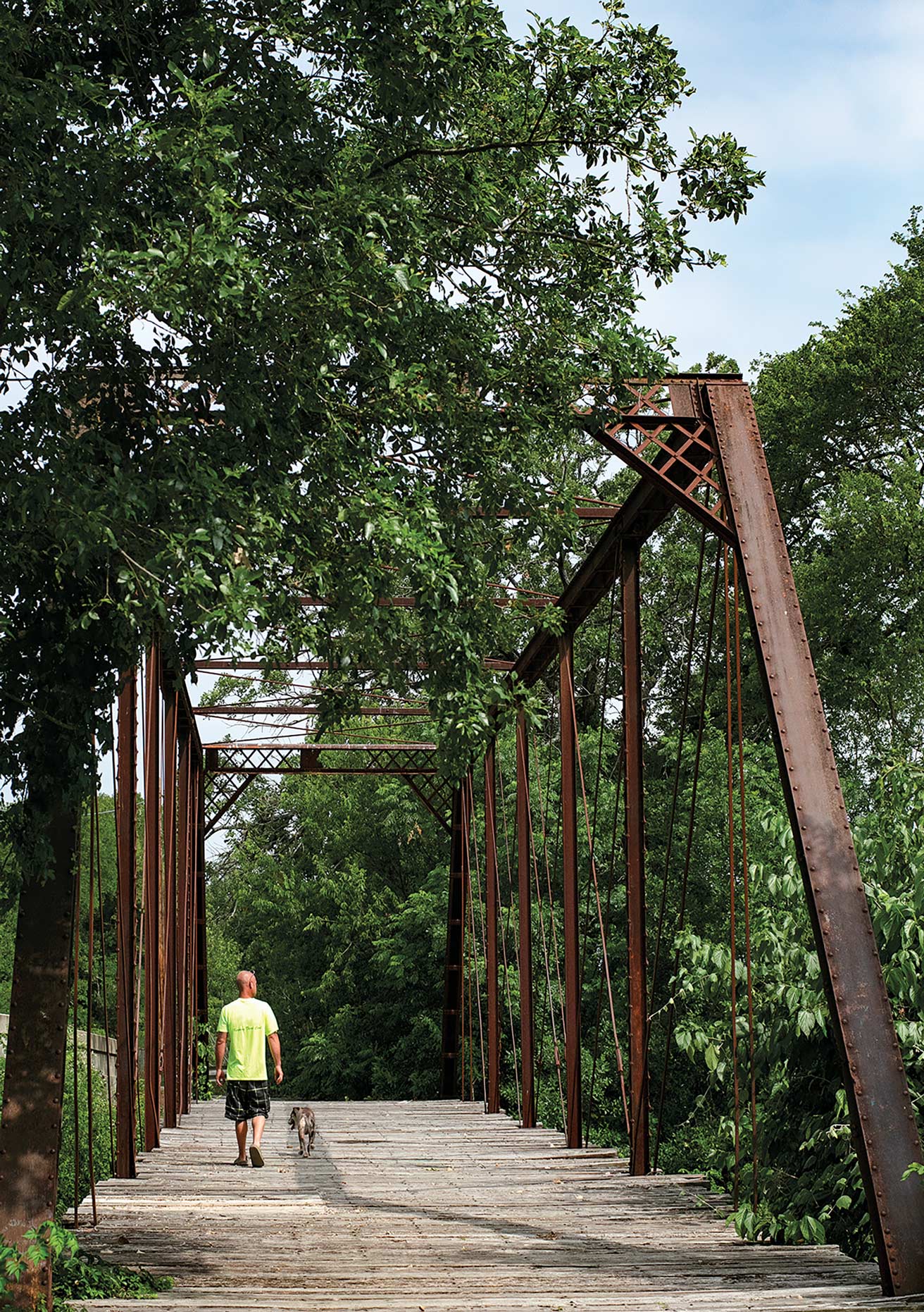 A man walking his dog across the Aquilla Creek iron truss bridge