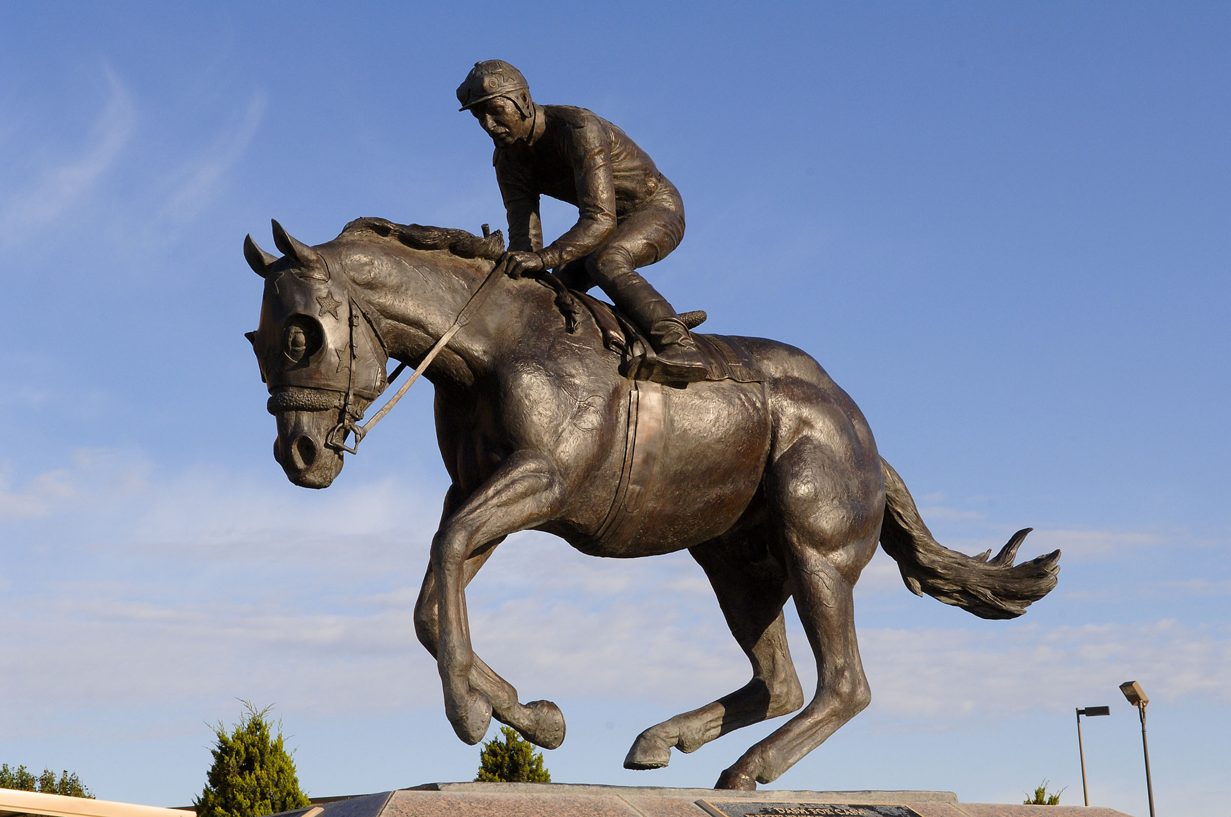 A bronze statue of a person riding a horse in front of blue sky