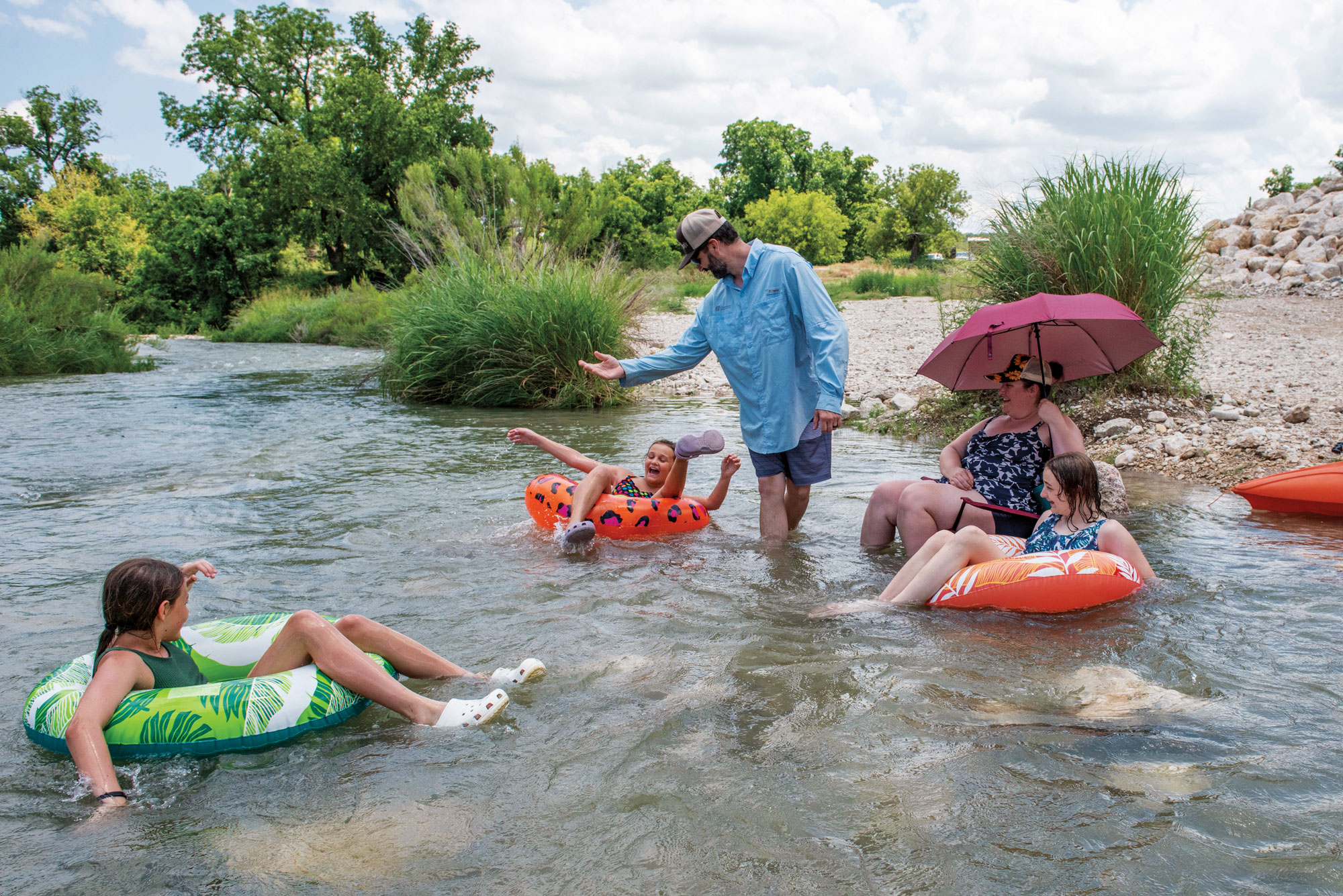 A man talks to children sitting in floaty tubes on a river