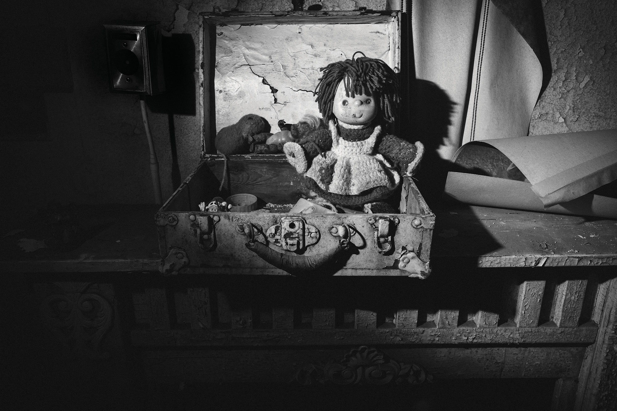 This high-contrast black and white photograph shows a creepy old-fashioned doll sitting on a mantle