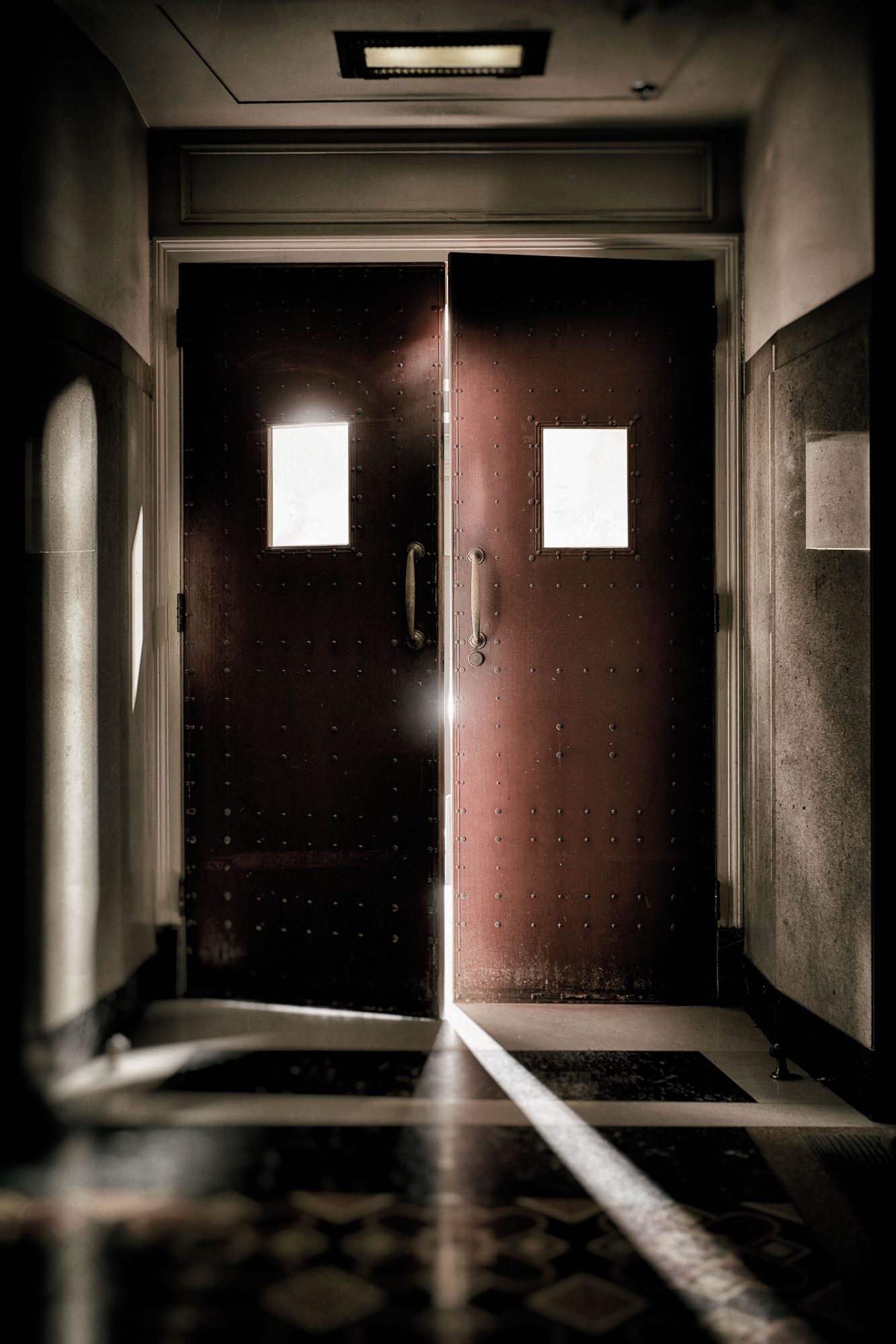 Two tall rust-colored doors with a crack of light showing through down a hallway