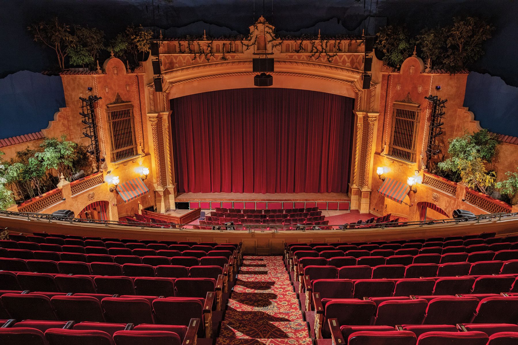 A view from above of an ornate, old-fashioned stage with golden lighting and a dark red curtain