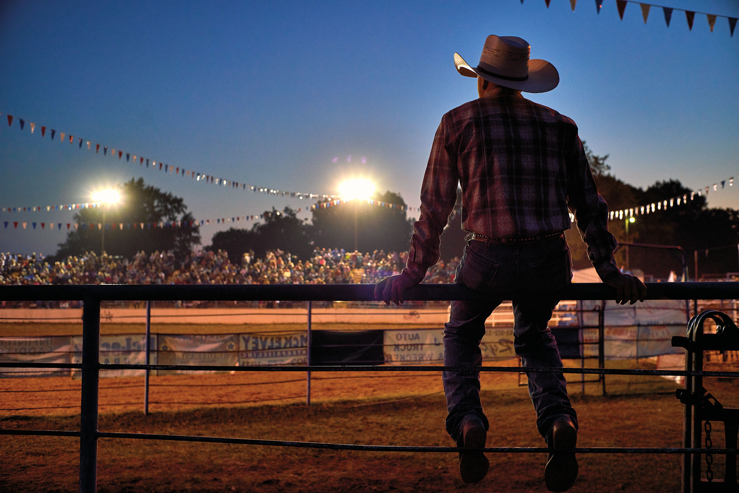 A man in a cowboy hat sits on a fence to watch the events at the Naples Watermelon Festival and Rodeo