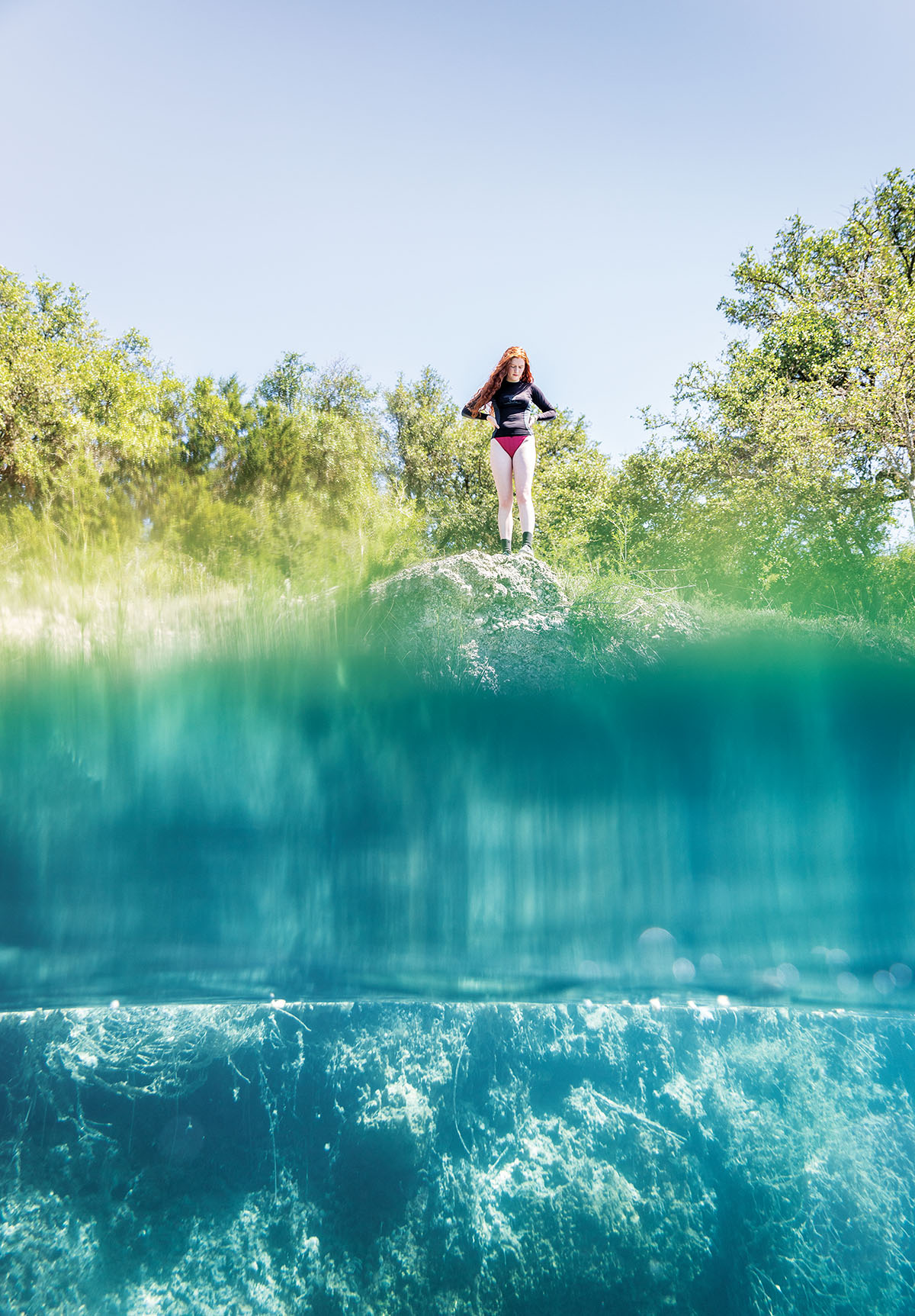 A young woman looks down into a swimming hole on the Nueces River