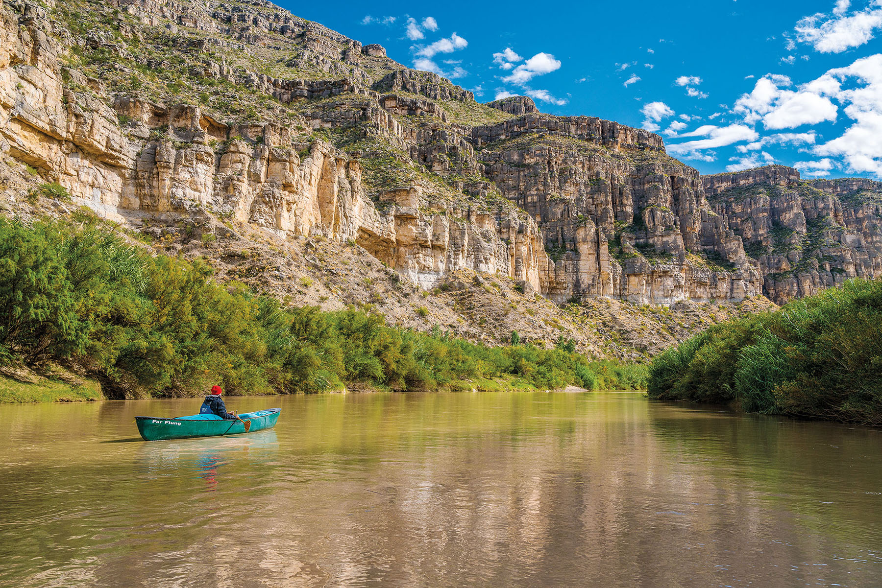 A teal canoe paddles between tall cliffs of the Rio Grande around Mile 737 in the Lower Canyons