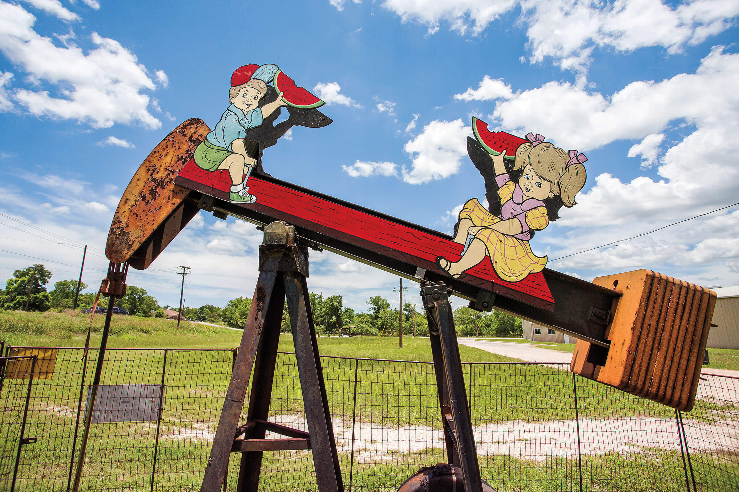A decorated pump jack where two children eating watermelon play like the pump jack is a seesaw
