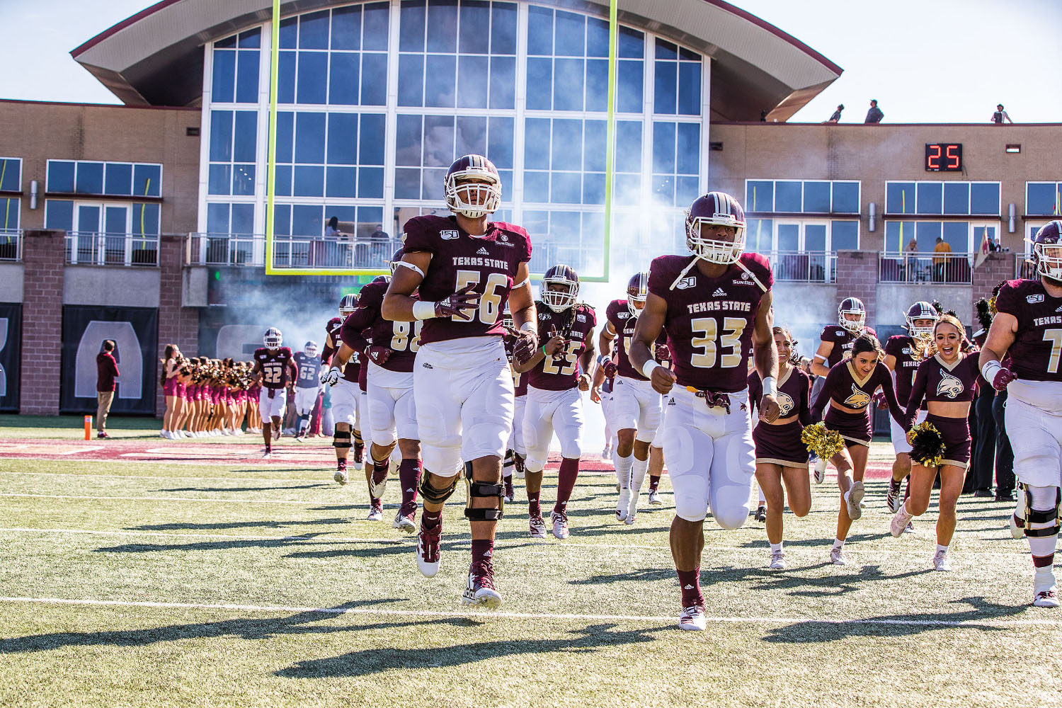 Football players and cheerleaders from Texas State take the field