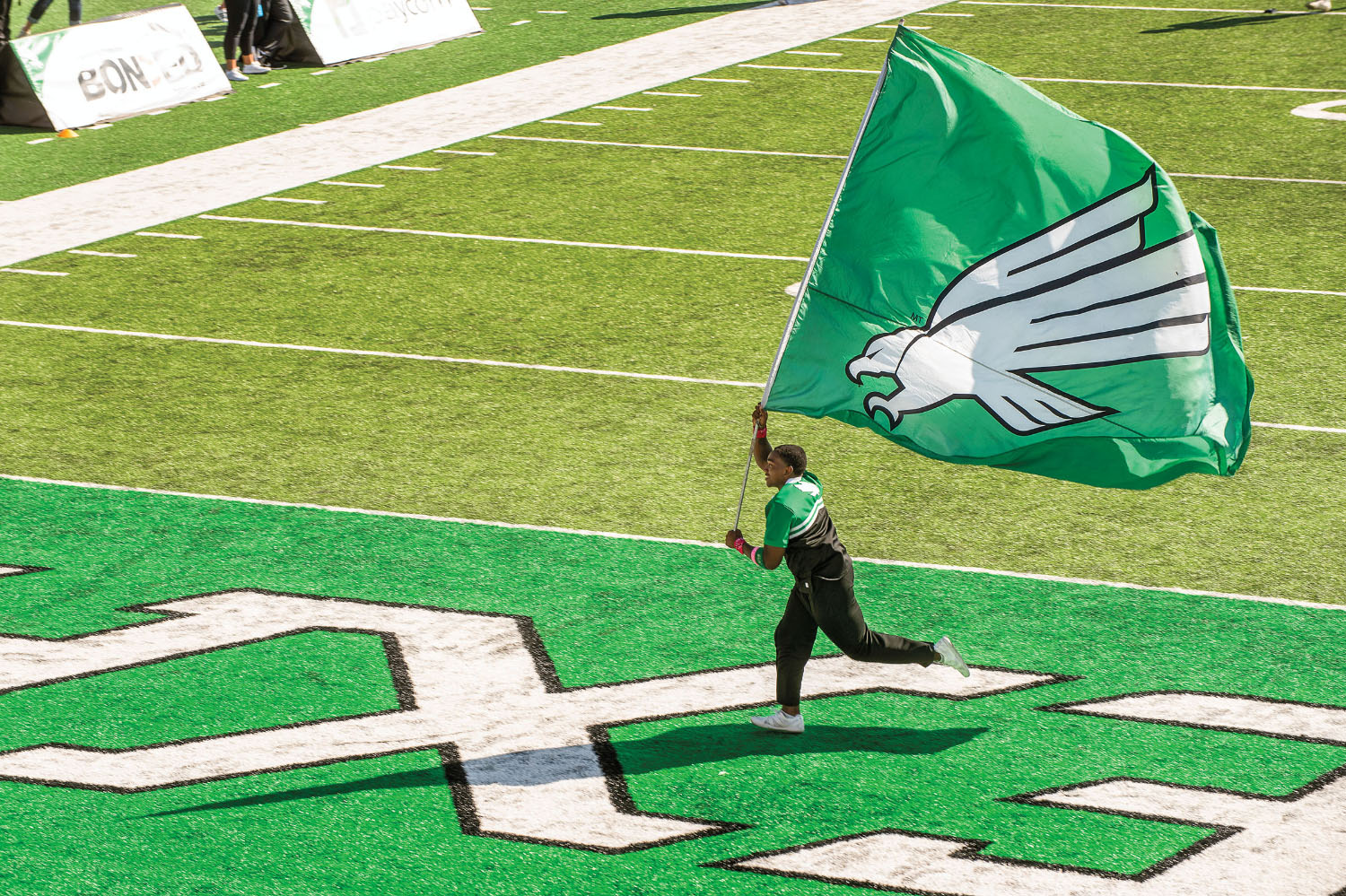 A man carries a large flag displaying the University of North Texas' logo and signature green color