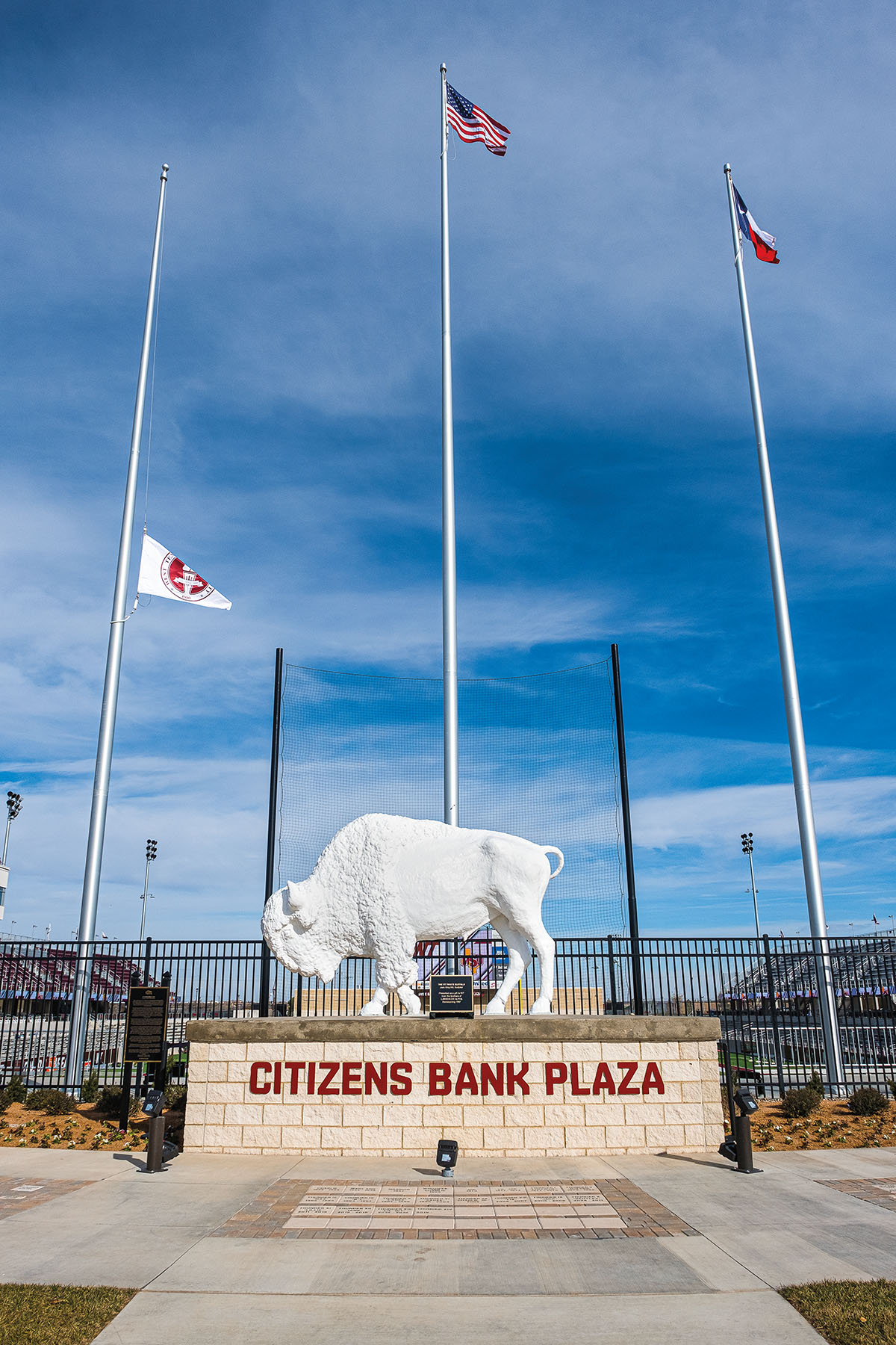 Underneath three flags, a statue of West Texas A&M's buffalo mascot on a platform reading "Citizens Bank Plaza"