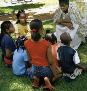 Children gather around a lady on the grass
