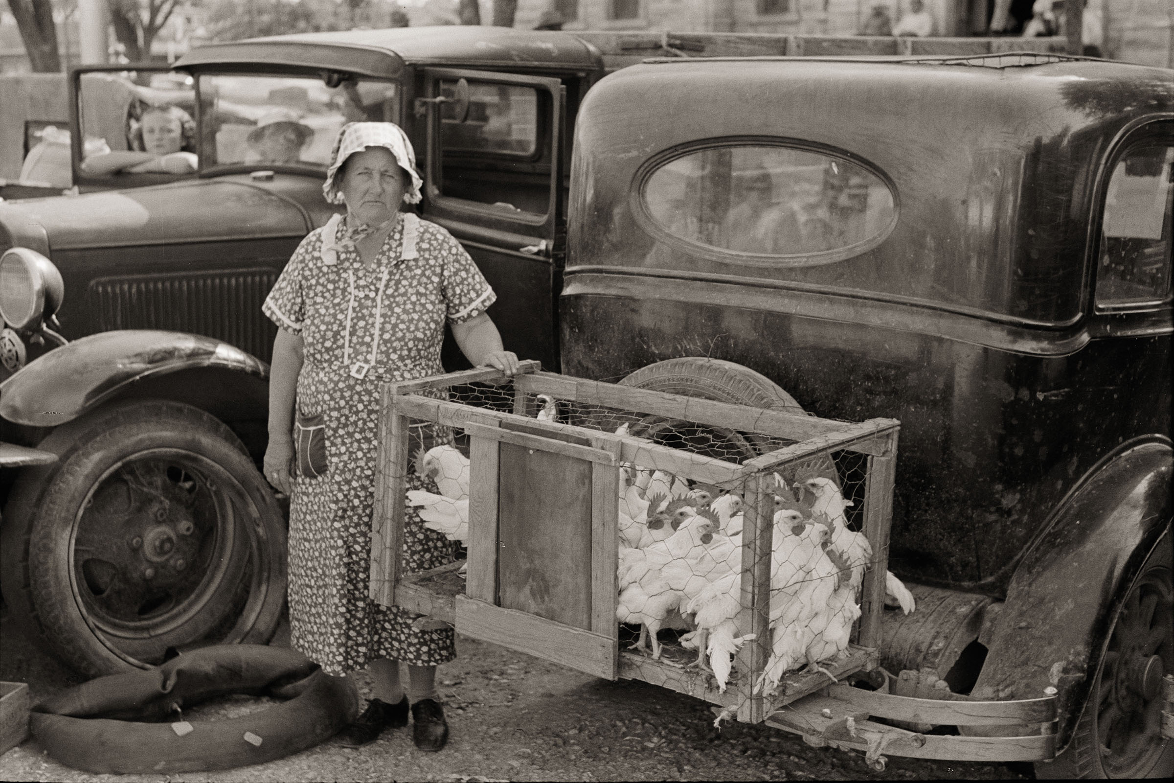 A vintage photo of a woman standing next to chickens on the back of a car at the Weatherford Trade Days