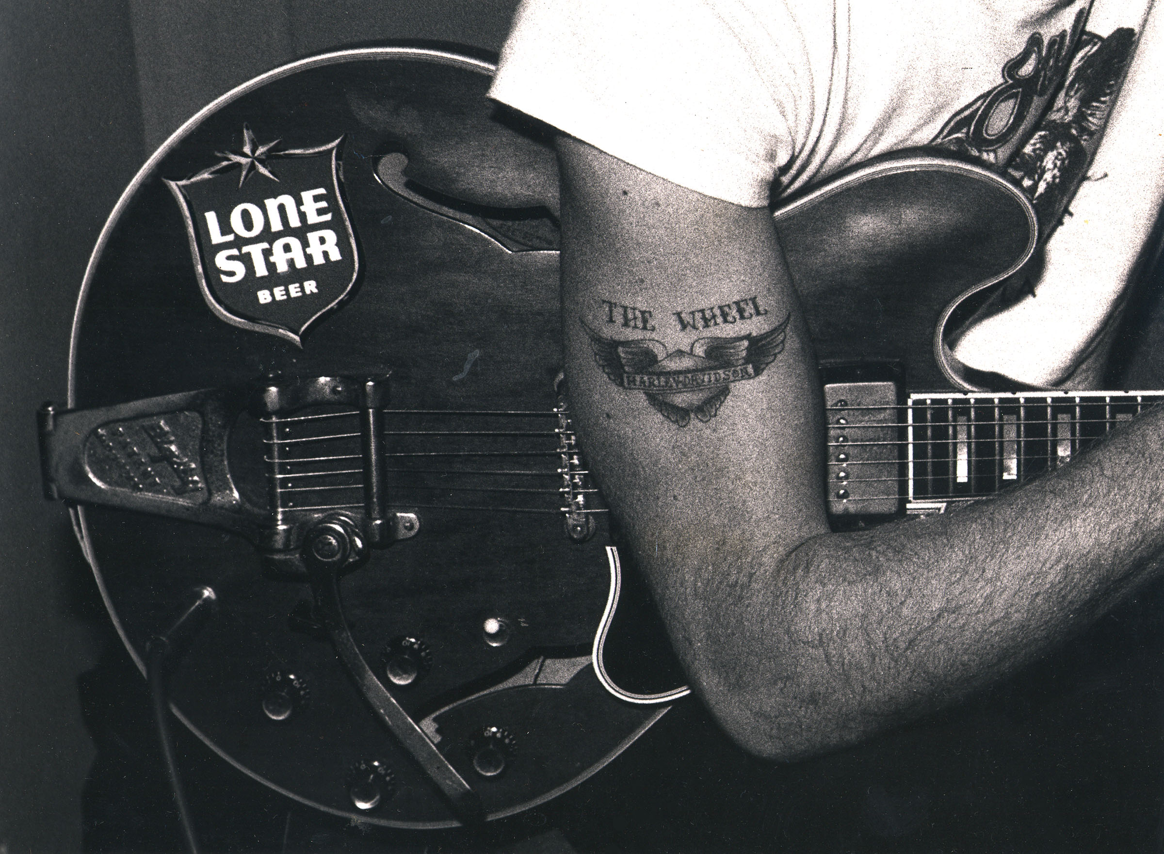 Ray Benson's arm over a guitar with an "Asleep at the Wheel" tattoo visible
