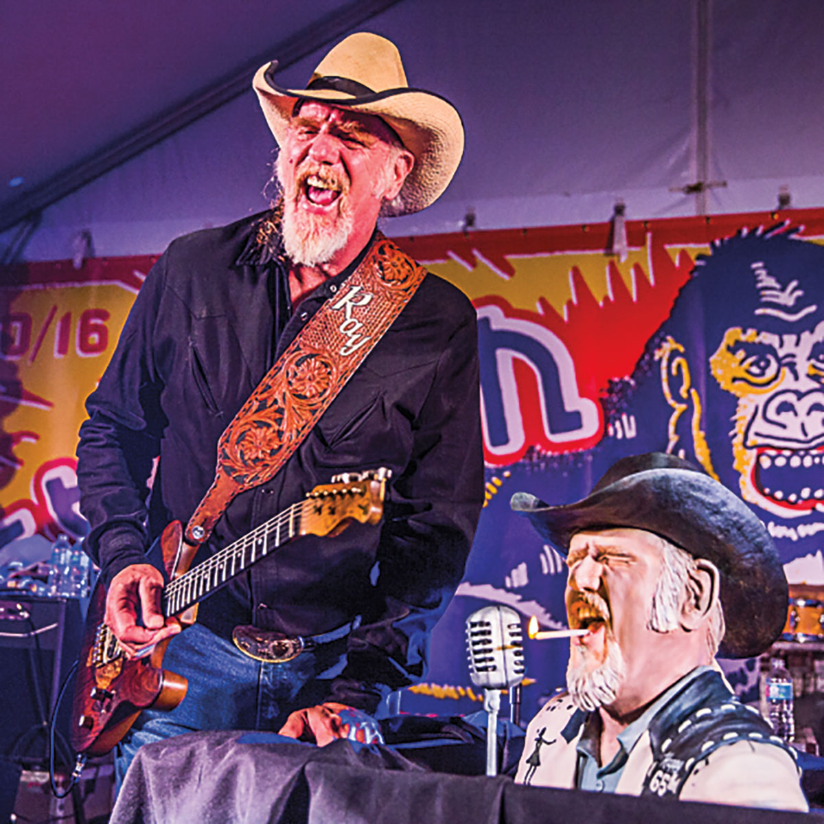 Ray Benson, in a cowboy hat and holding a guitar, poses just like a lookalike cake of him