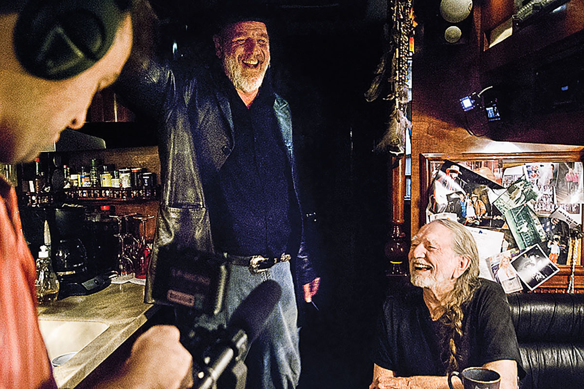 Ray Benson and Willie Nelson laugh inside of a tour bus