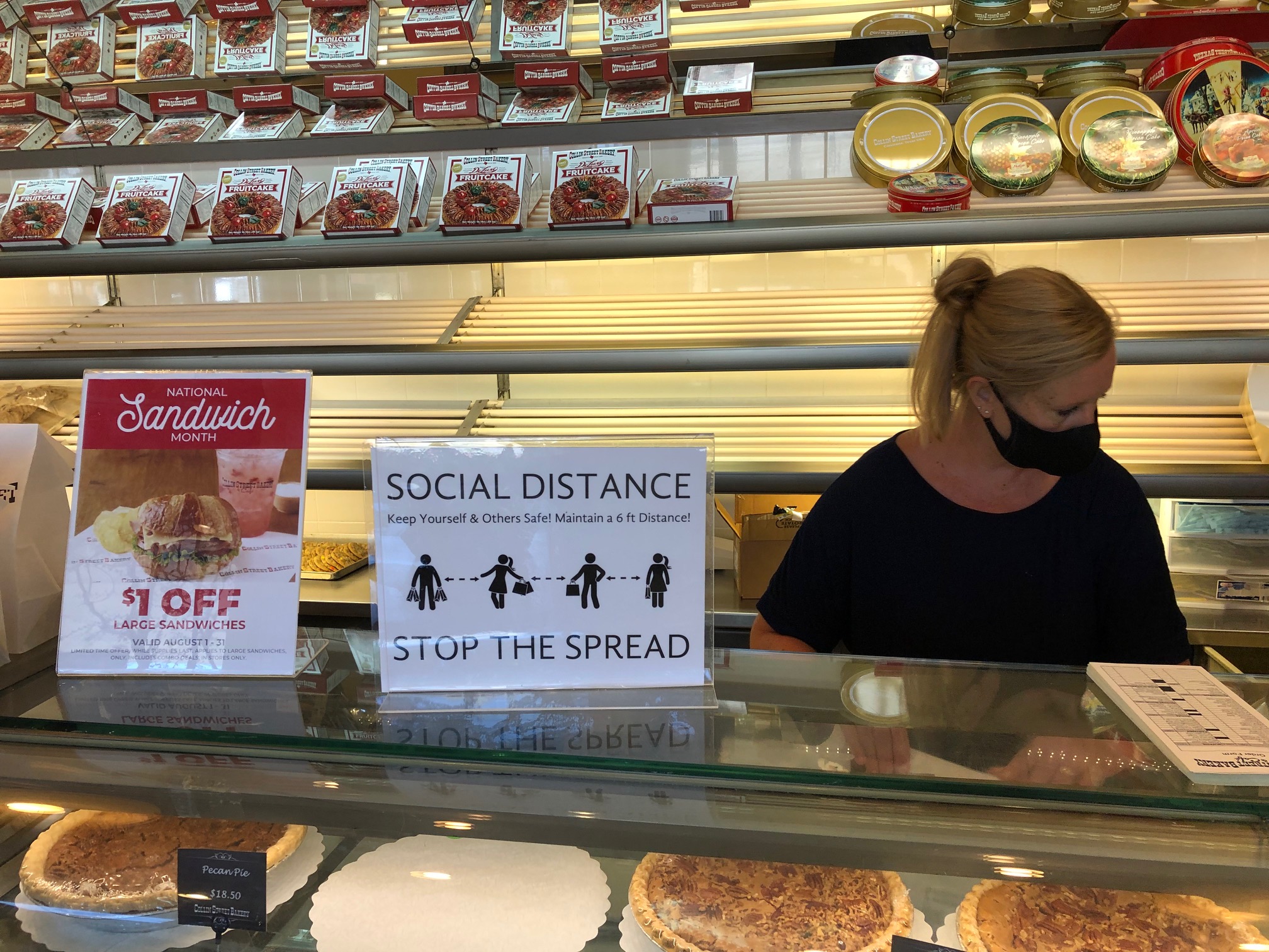 Woman behind the counter at Collin Street Bakery wears a mask