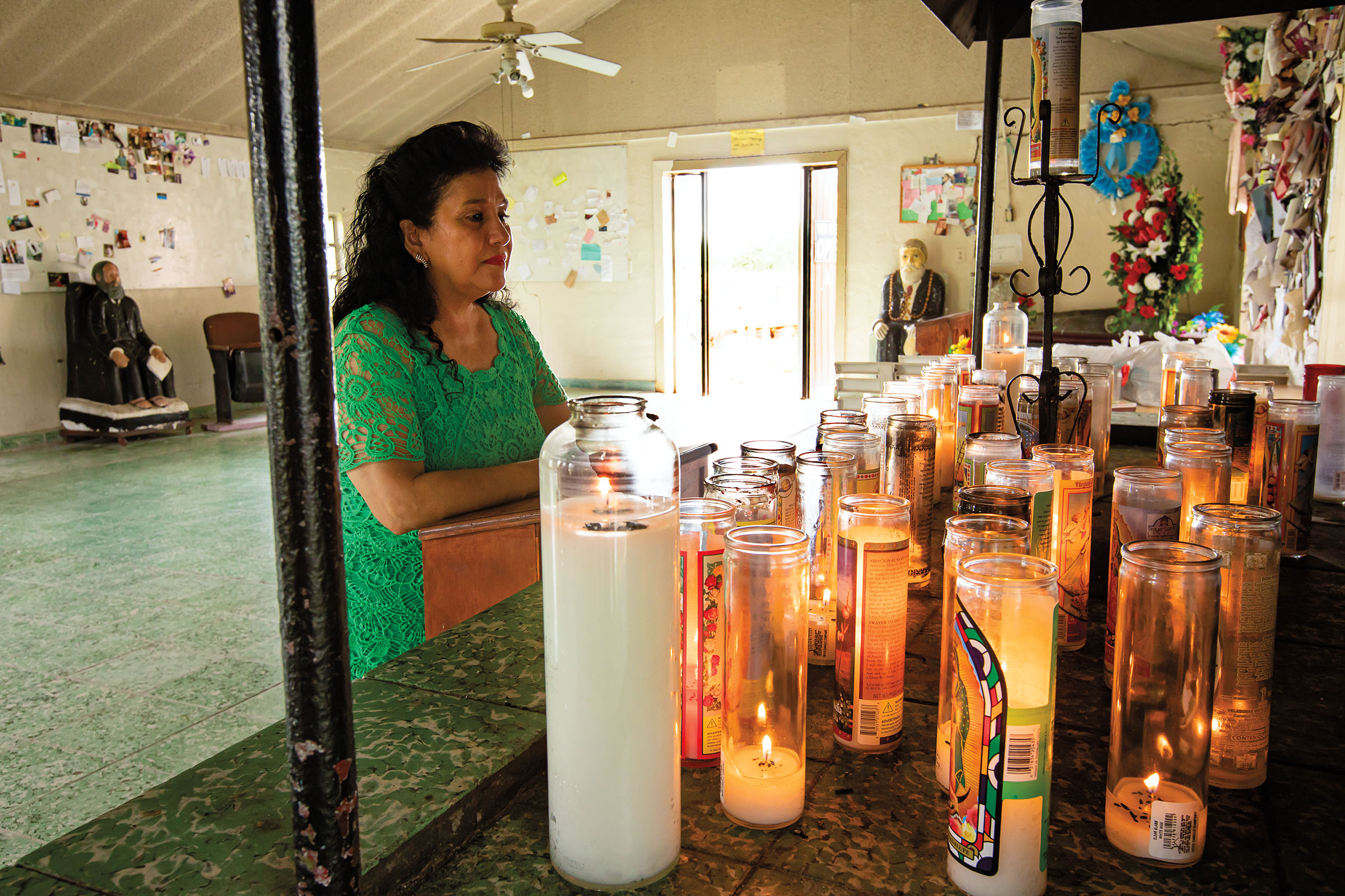 A woman in green stands before an altar of lit candles