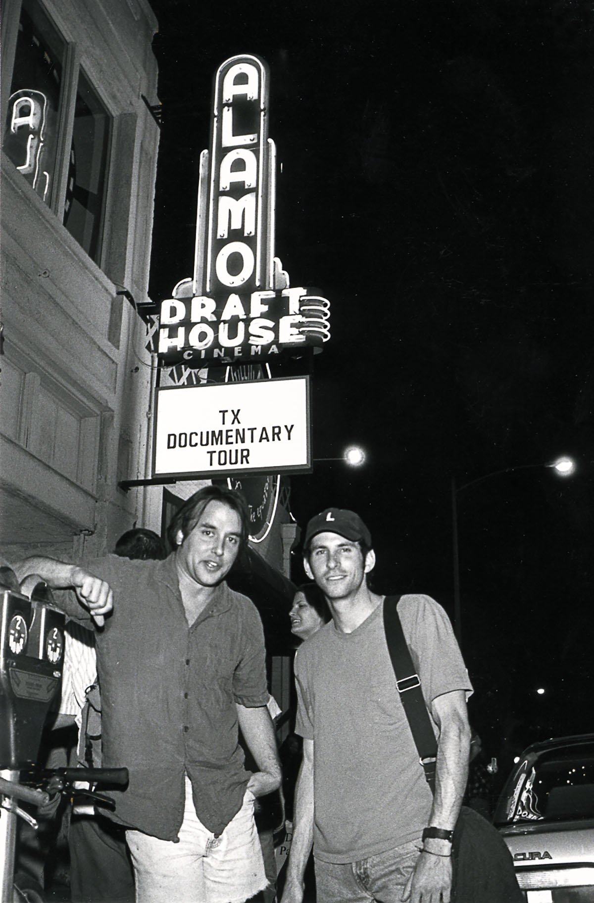Richard Linklater poses outside the Alamo Drafthouse Cinema in Austin beneath a sign reading "TX Documentary Tour"
