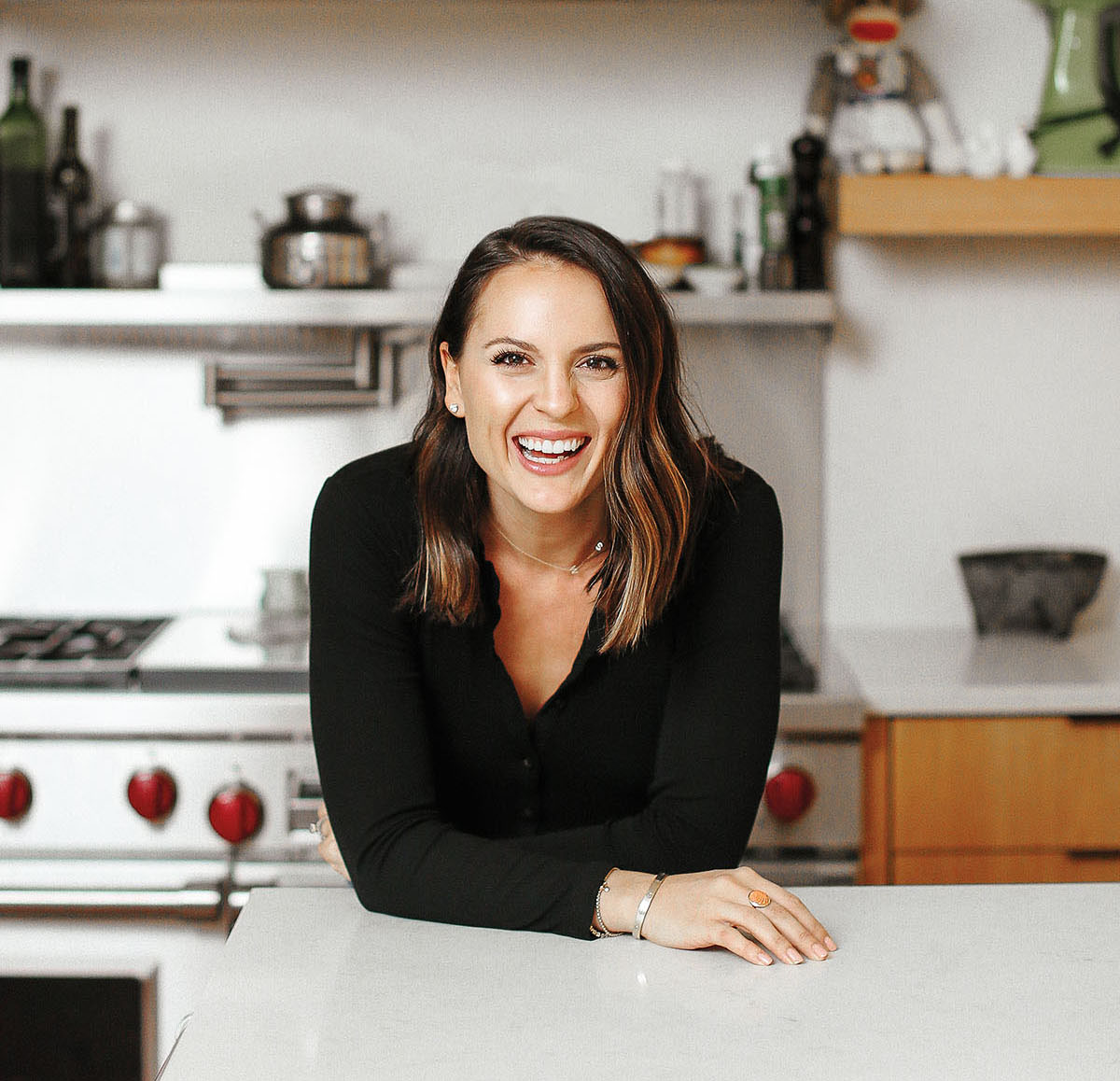 A photo of Alex Snodgrass in her kitchen, in front of a stainless steel gas range and resting her arm on a quartz countertop