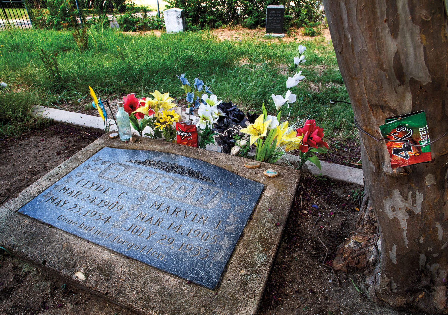 Clyde's gravestone, adorned with flowers and a bag of Doritos