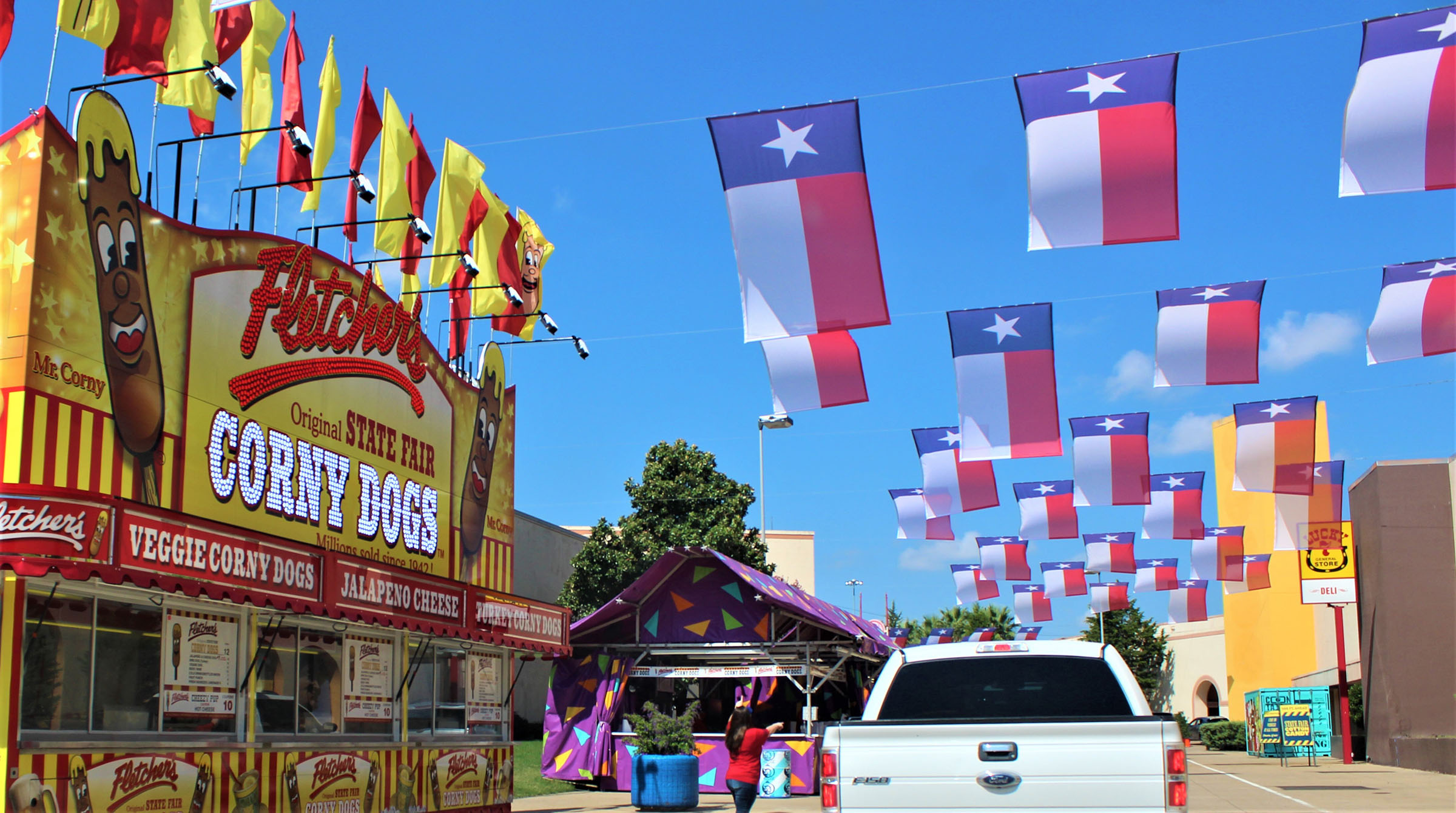 Texas flags fly above a line of cars next to Fletchers State Fair Corny Dogs stand