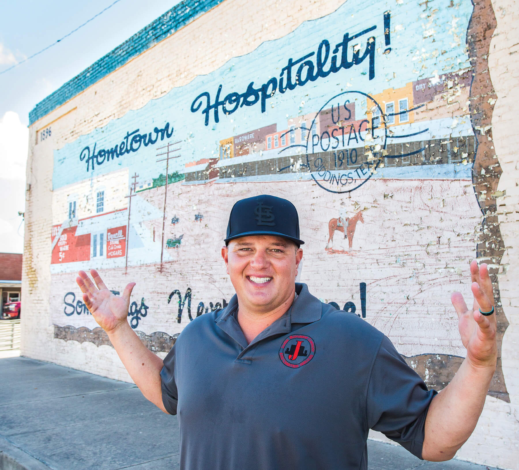 Jacob Janda stands in front of a mural in Giddings reading "Hometown Hospitality"