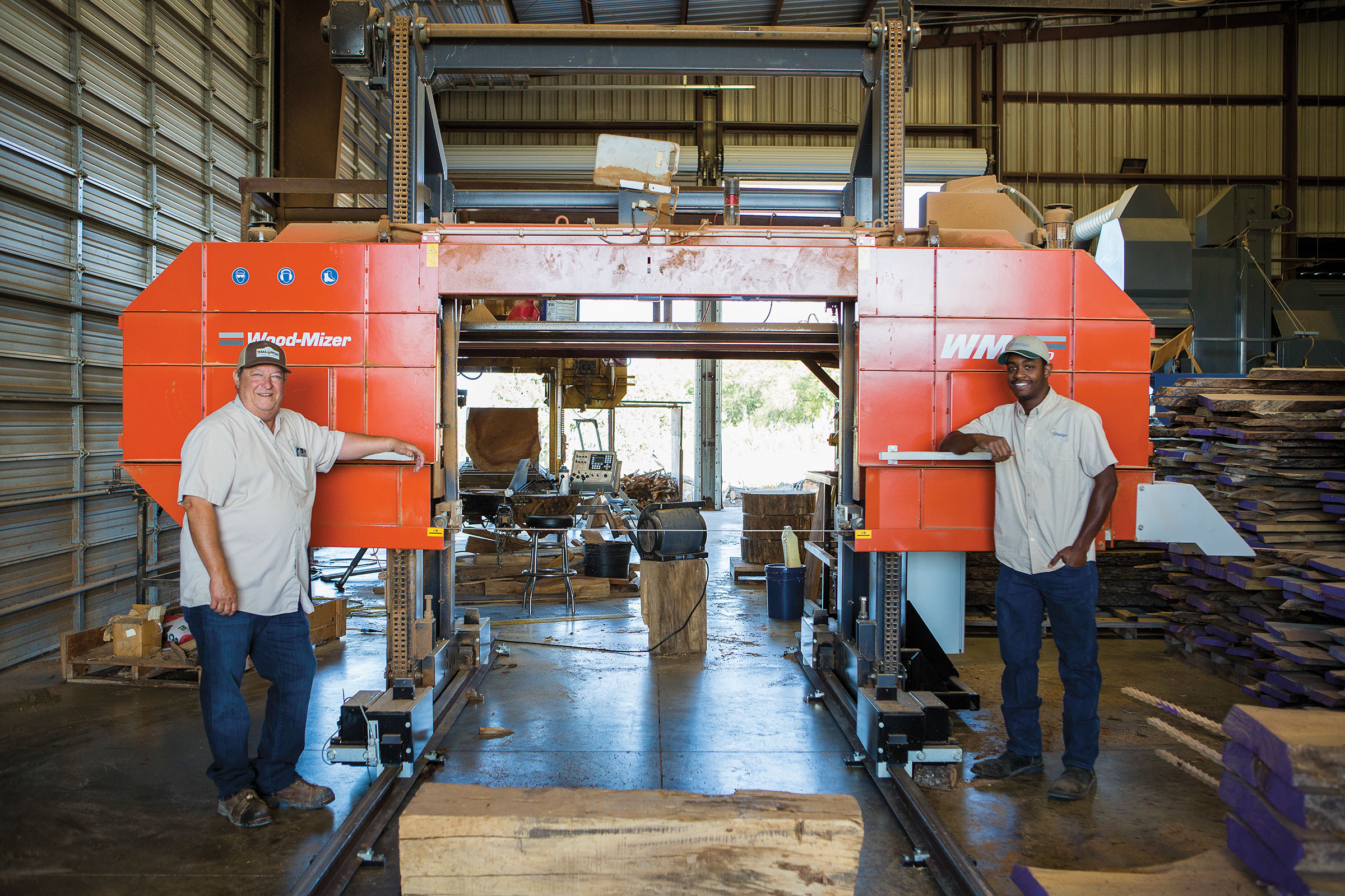 Two men stand in front of a bright orange machine labed "Wood-Mizer"