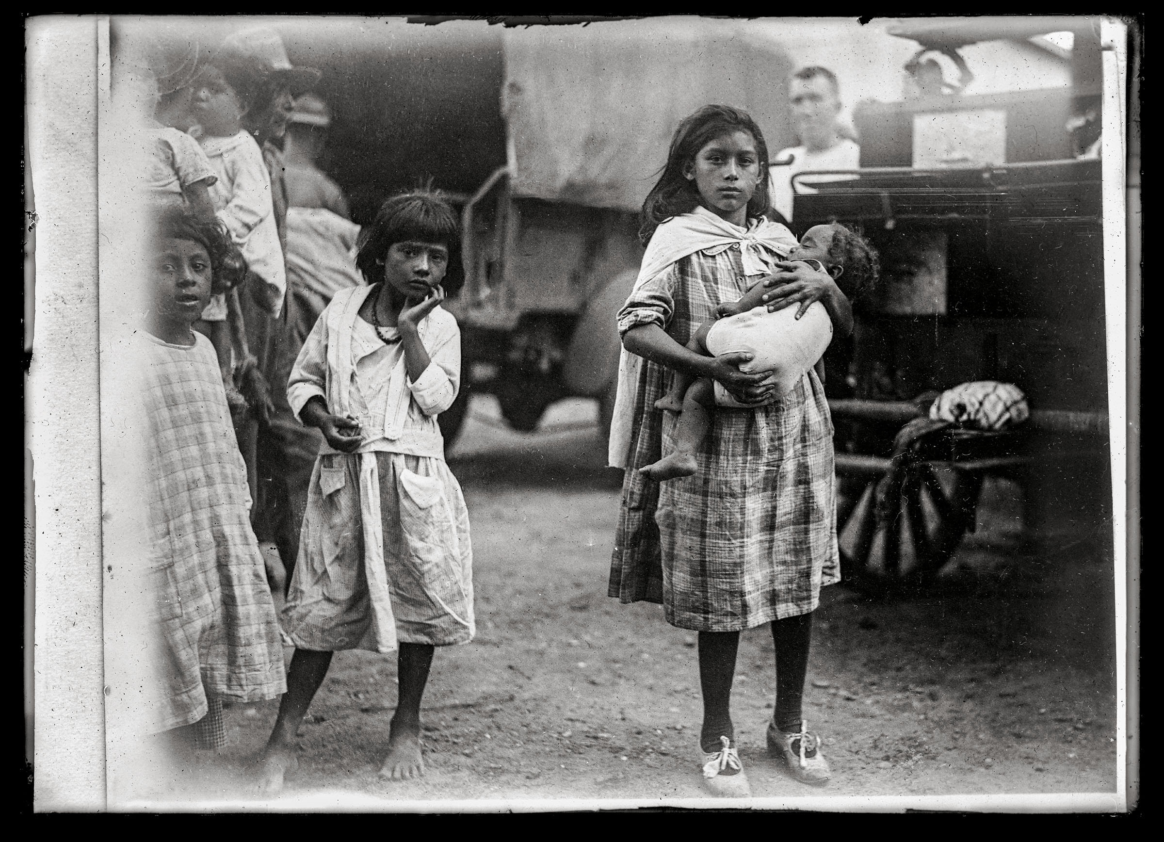 Children, one of which holds a baby, stand in front of a wagon