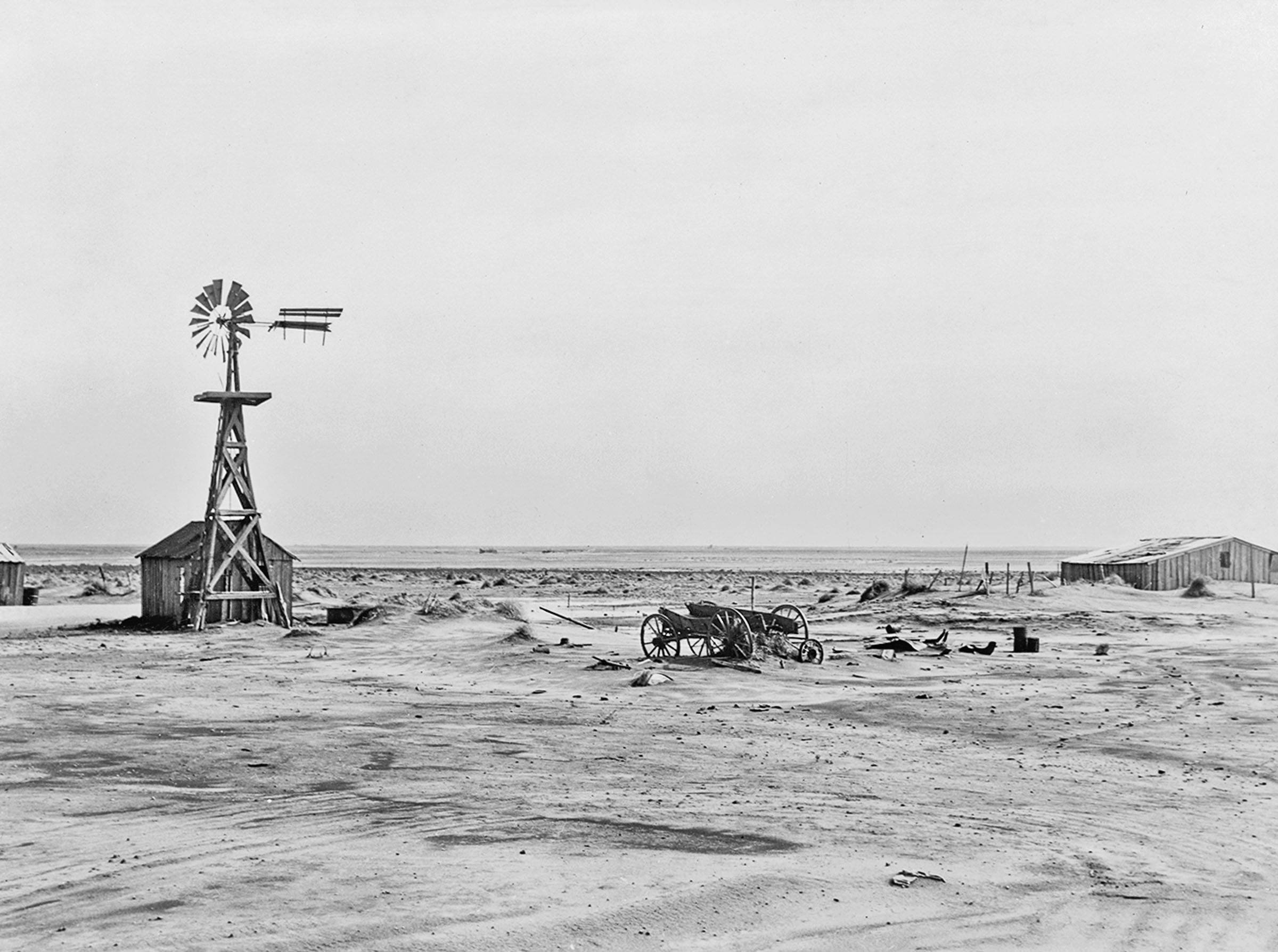A farm with a large windmill behing hit by a dust storm