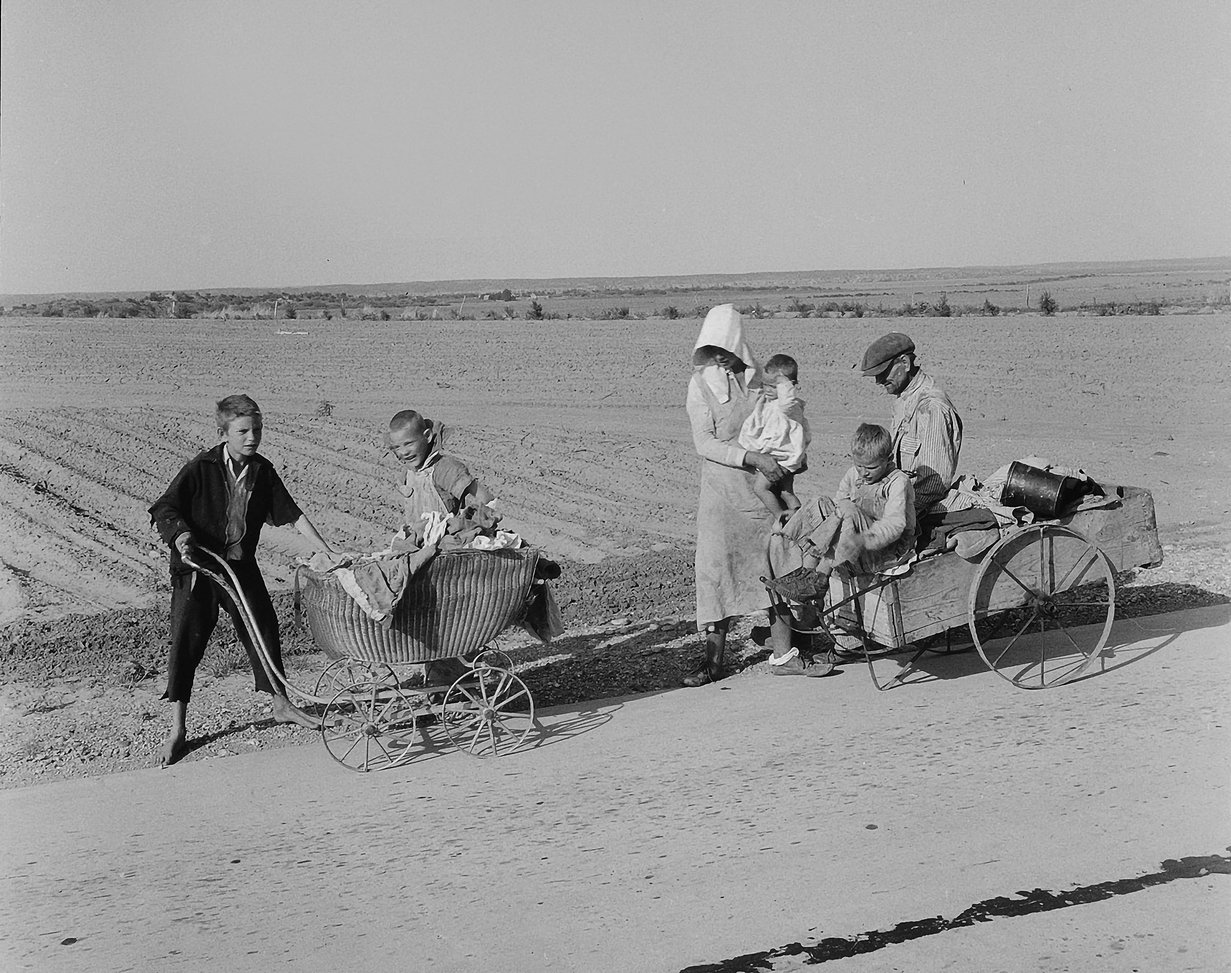 A family with all of their belongings stands by the side of a dusty road