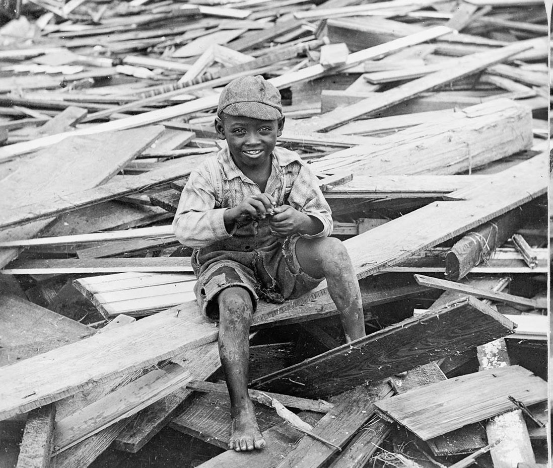 A young boy in a hat sits in a pile of rubble