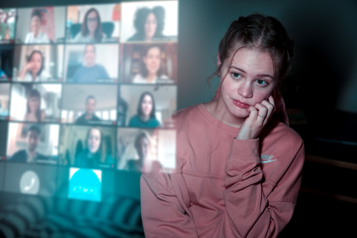 A young woman looks at the reflection of several faces on a Zoom call