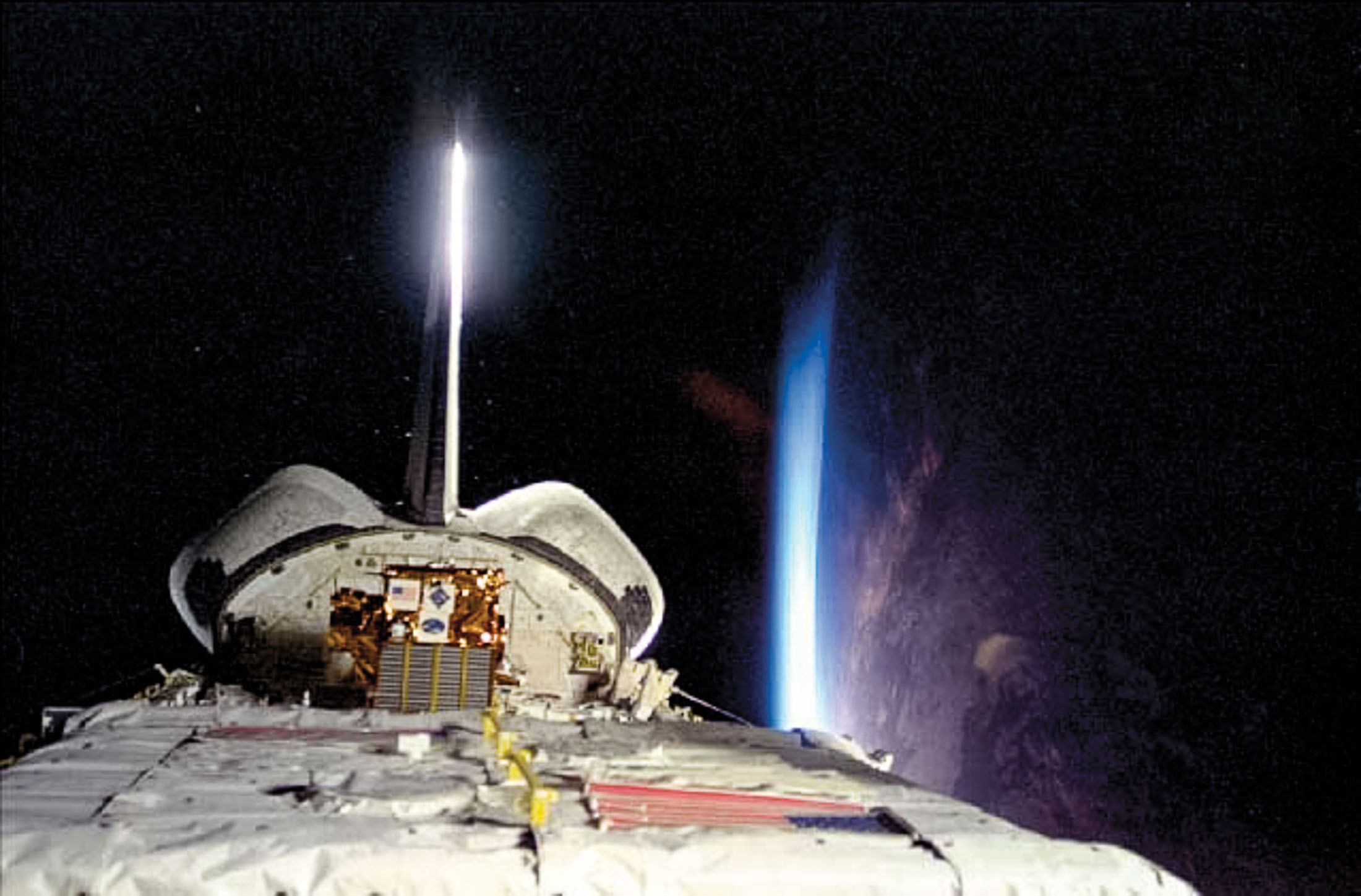 Top view of Space Shuttle Discovery with engines firing and the Earth in the background