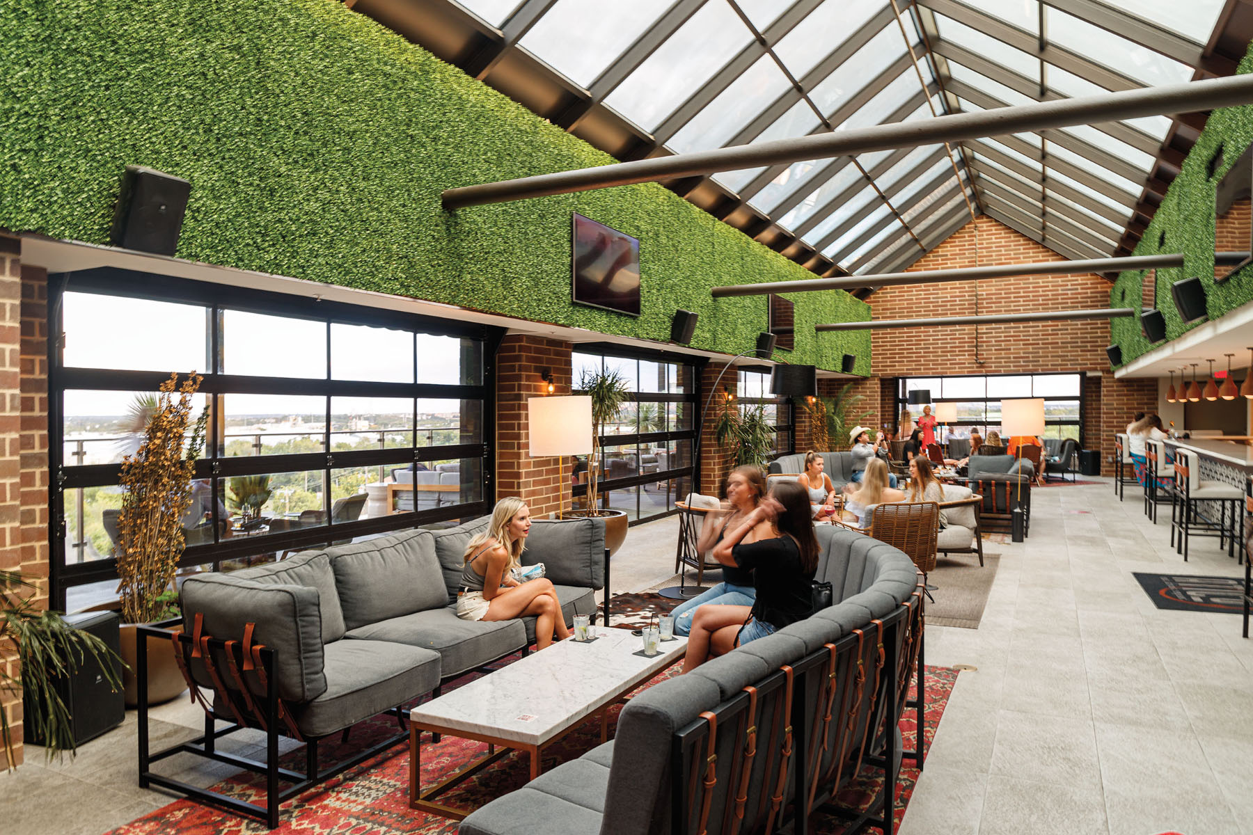 Diners sit on gray outdoor furnature under a grassy wall and bright, skylight-filled ceiling