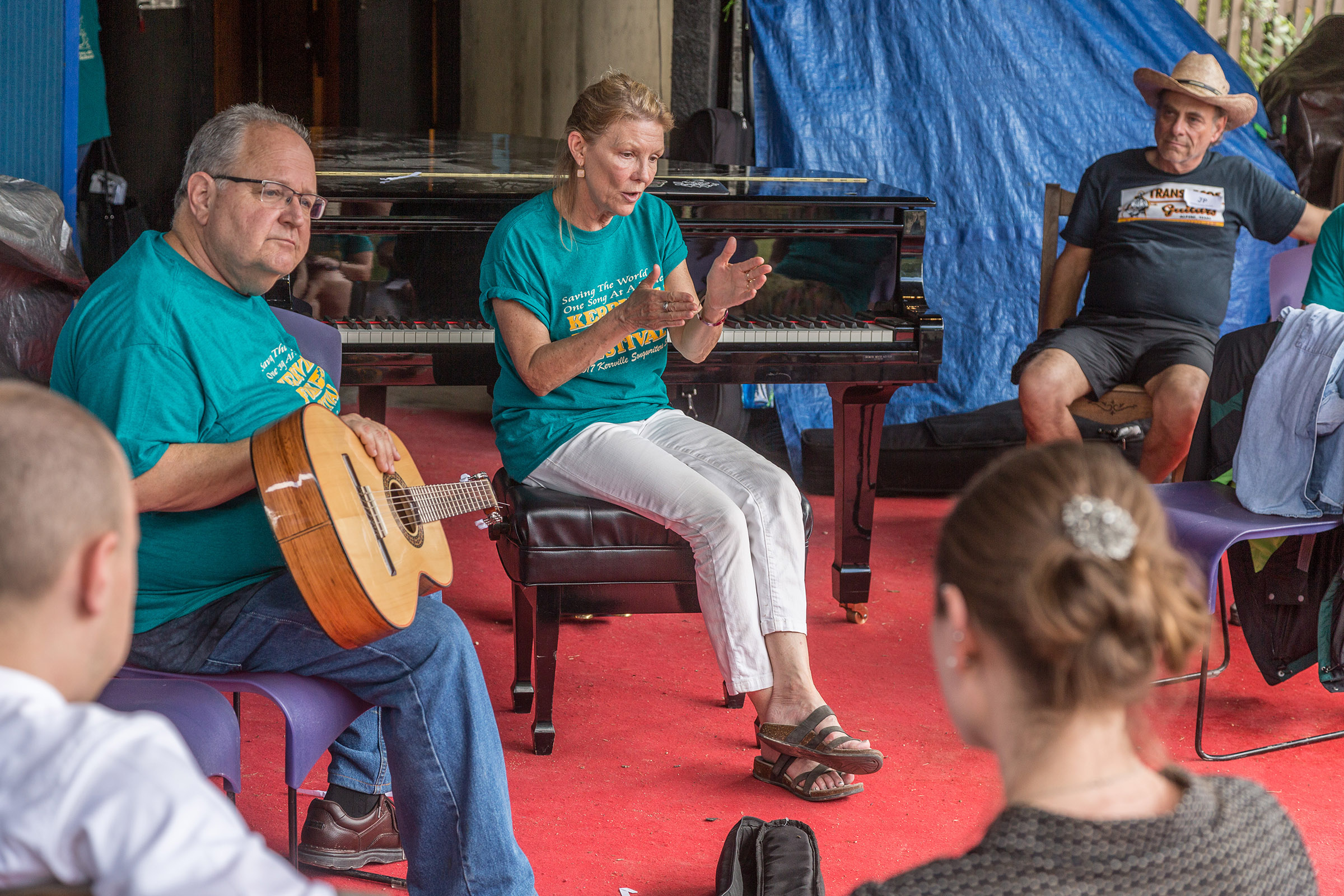 A man with a guitar and a woman expressing a thought with her hands work with songwriters in a circle