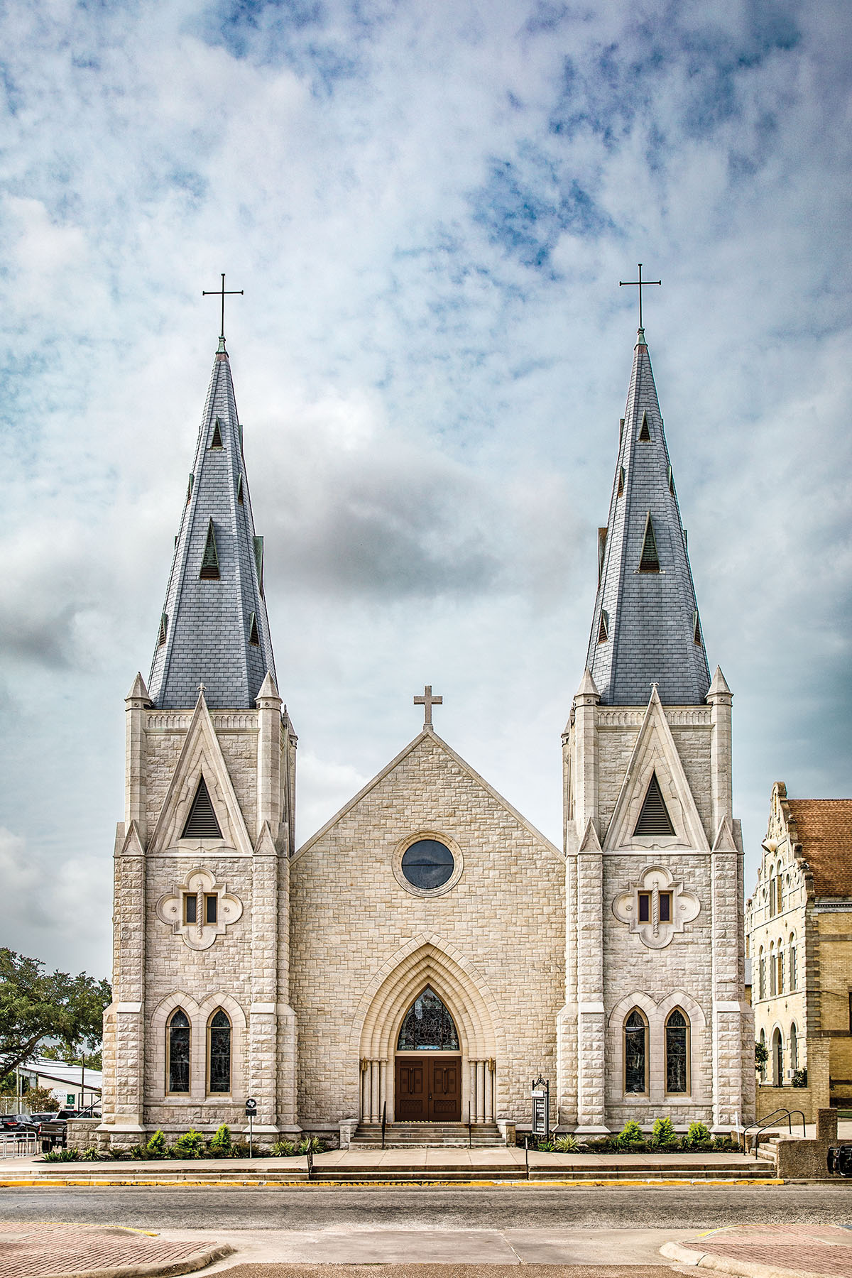 Stone and gray steeples of a church in front of a blue, cloudy sky