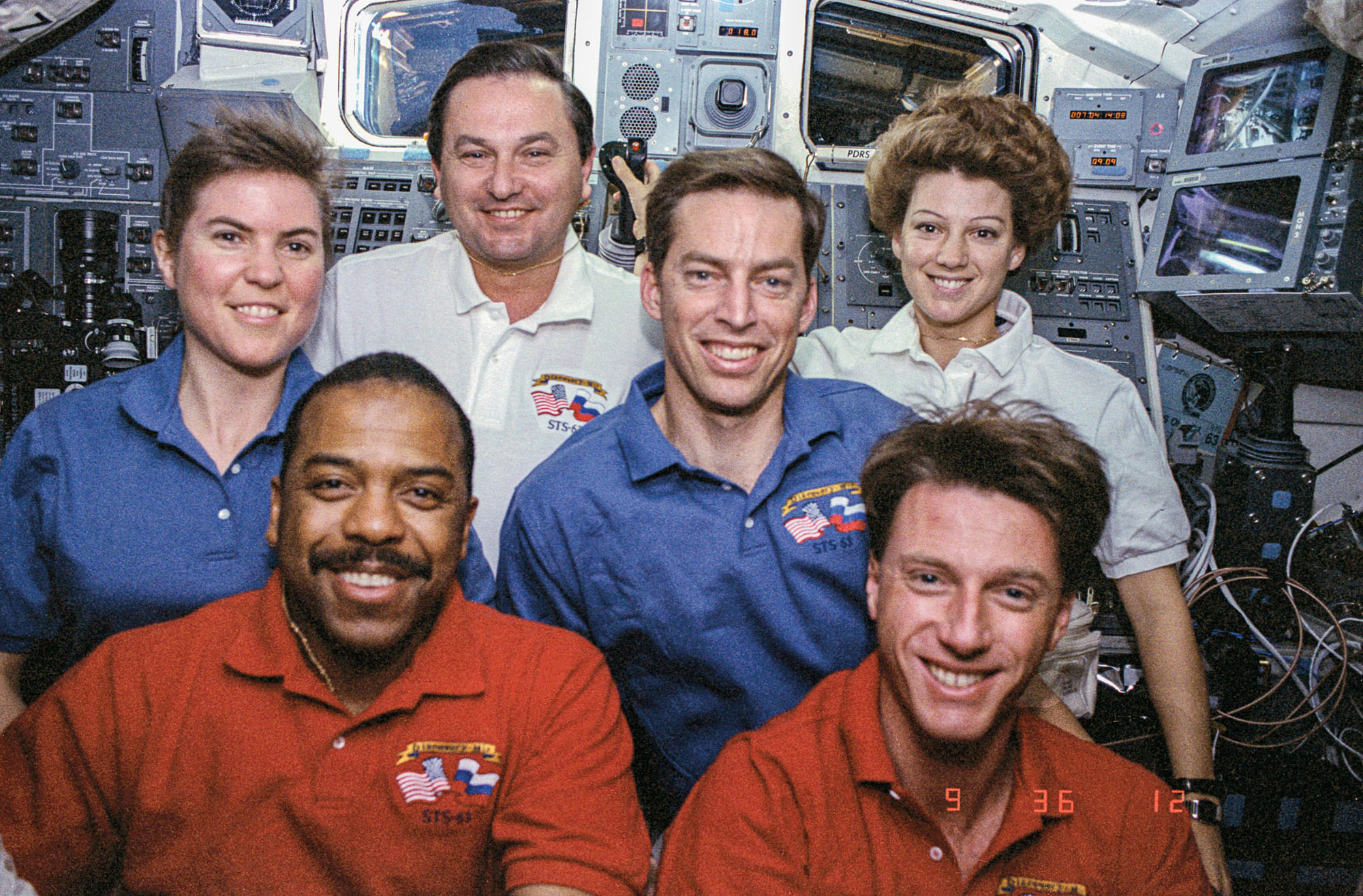 The crew looks smiling at the camera from inside the Space Shuttle
