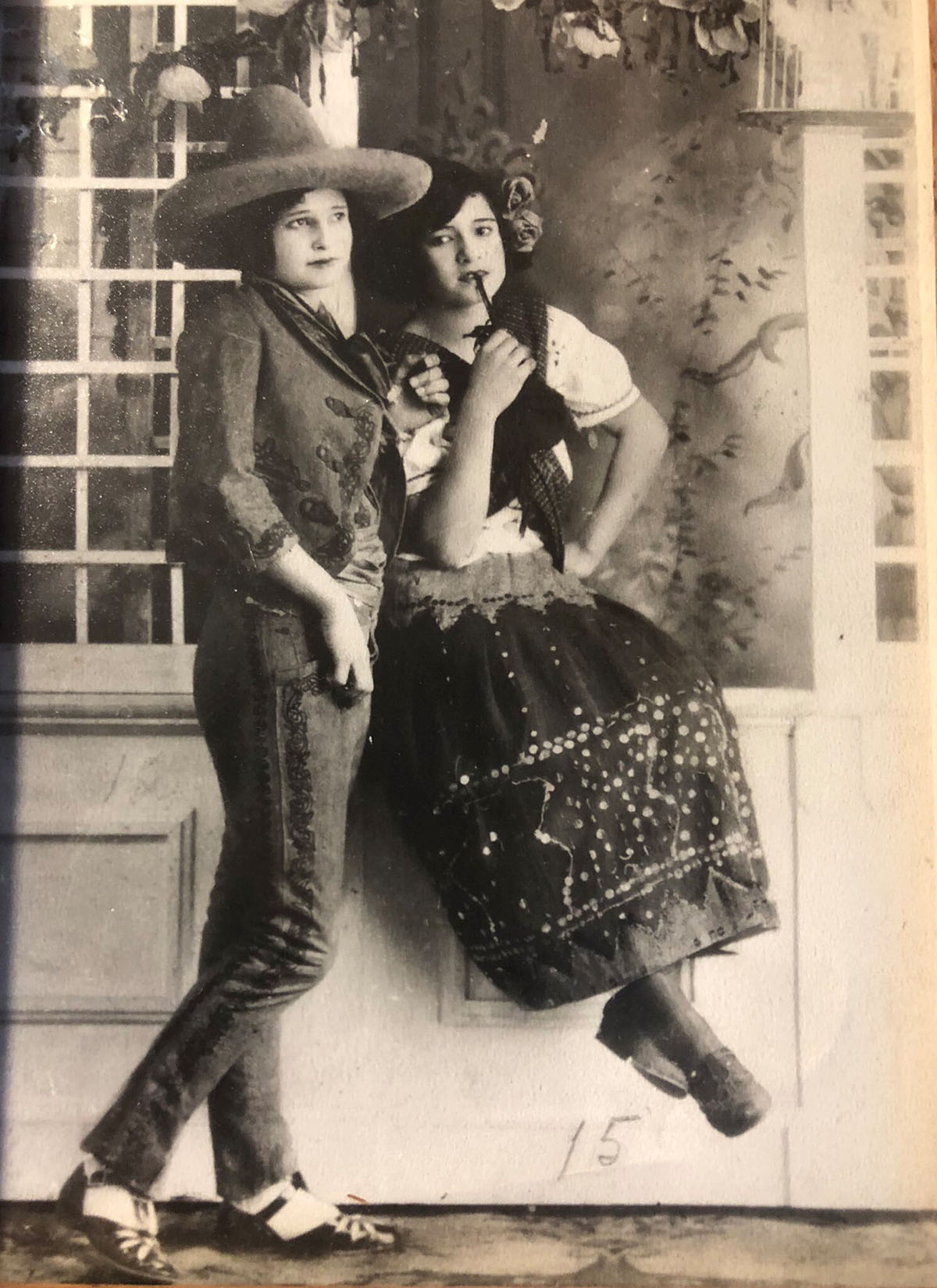 Two women in an old fashioned photograph sit on a wall