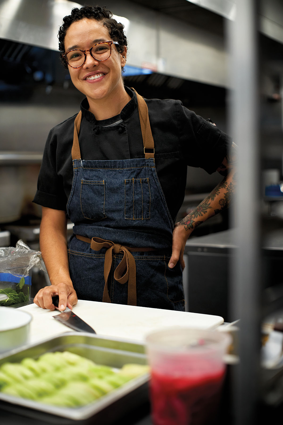 A woman in a blue apron stands behind a cutting board