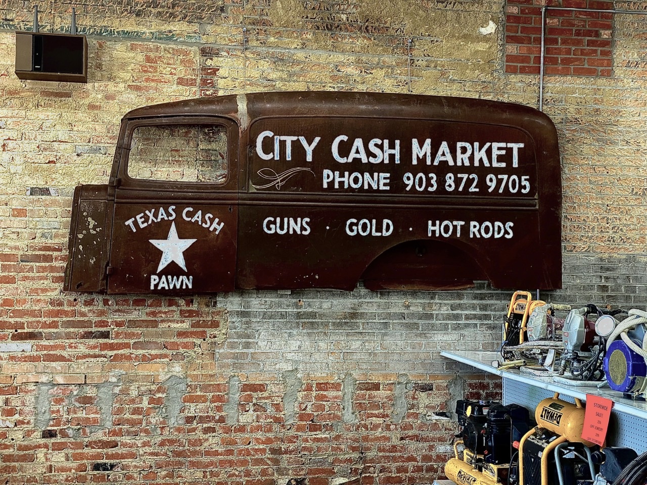 The side of an old metal truck painted with the words City Cash Market hangs on a brick wall. 