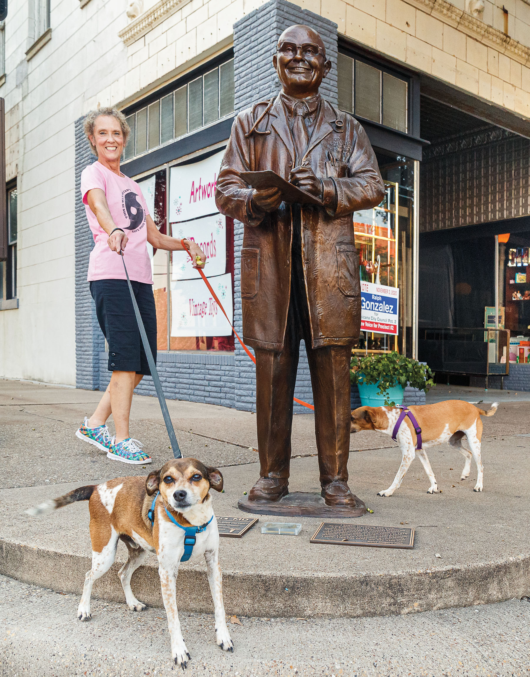 A woman walking dogs past a bronze sculpture of Dr. Kent Rogers