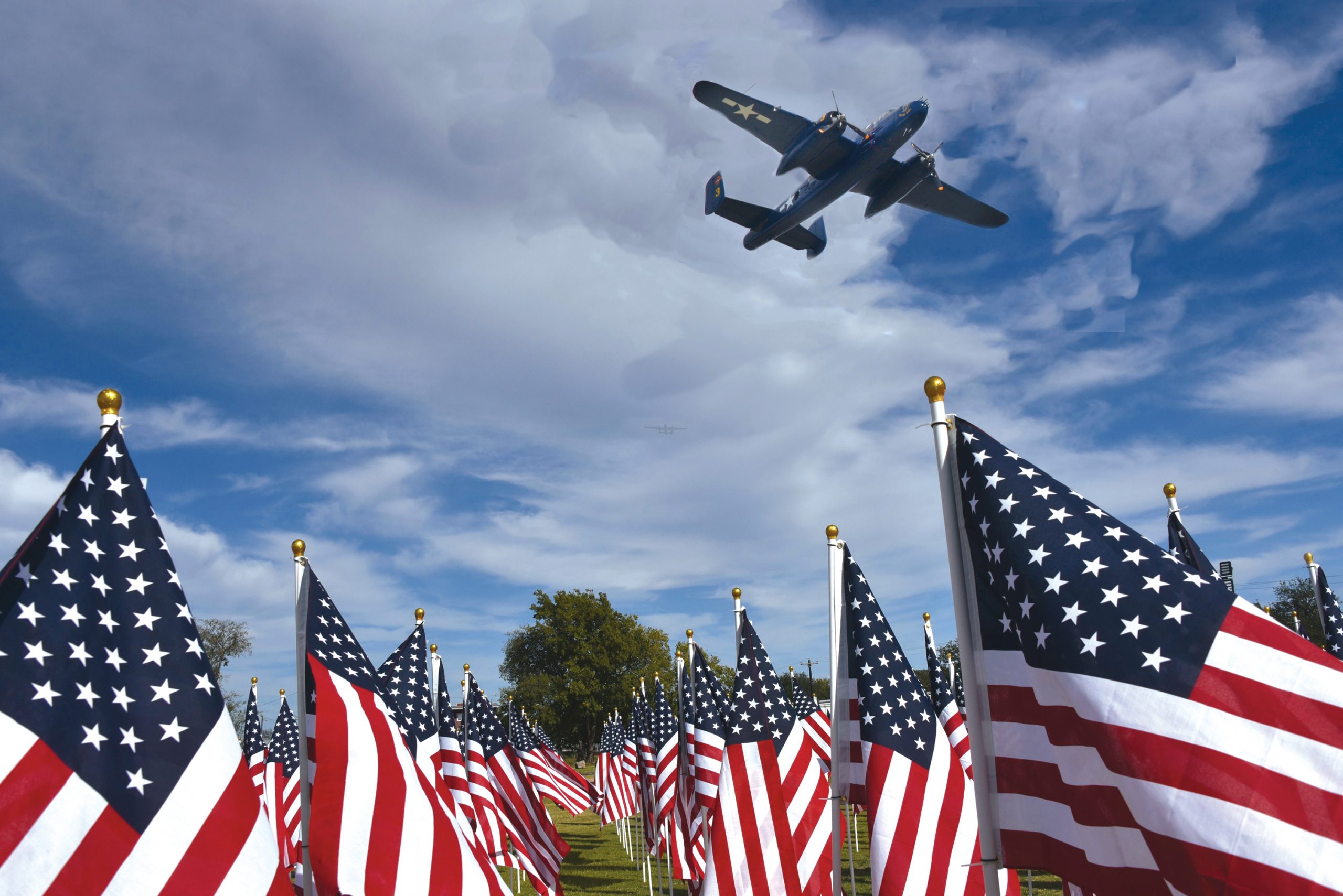 A military plane flies over a field of flags in Georgetown at the Field of Honor. 
