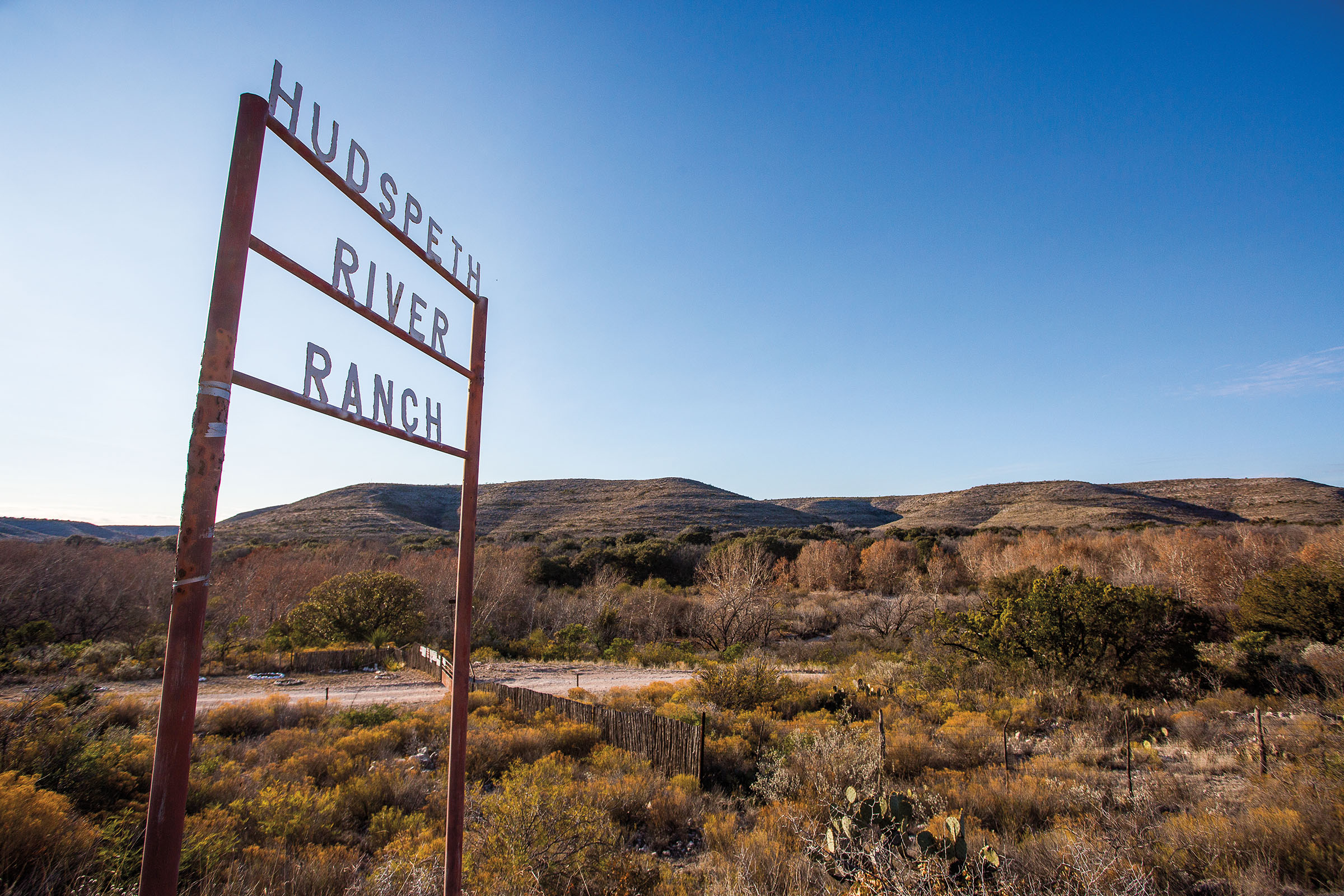 An iron sign reading "Hudspeth River Ranch" beneath a blue sky
