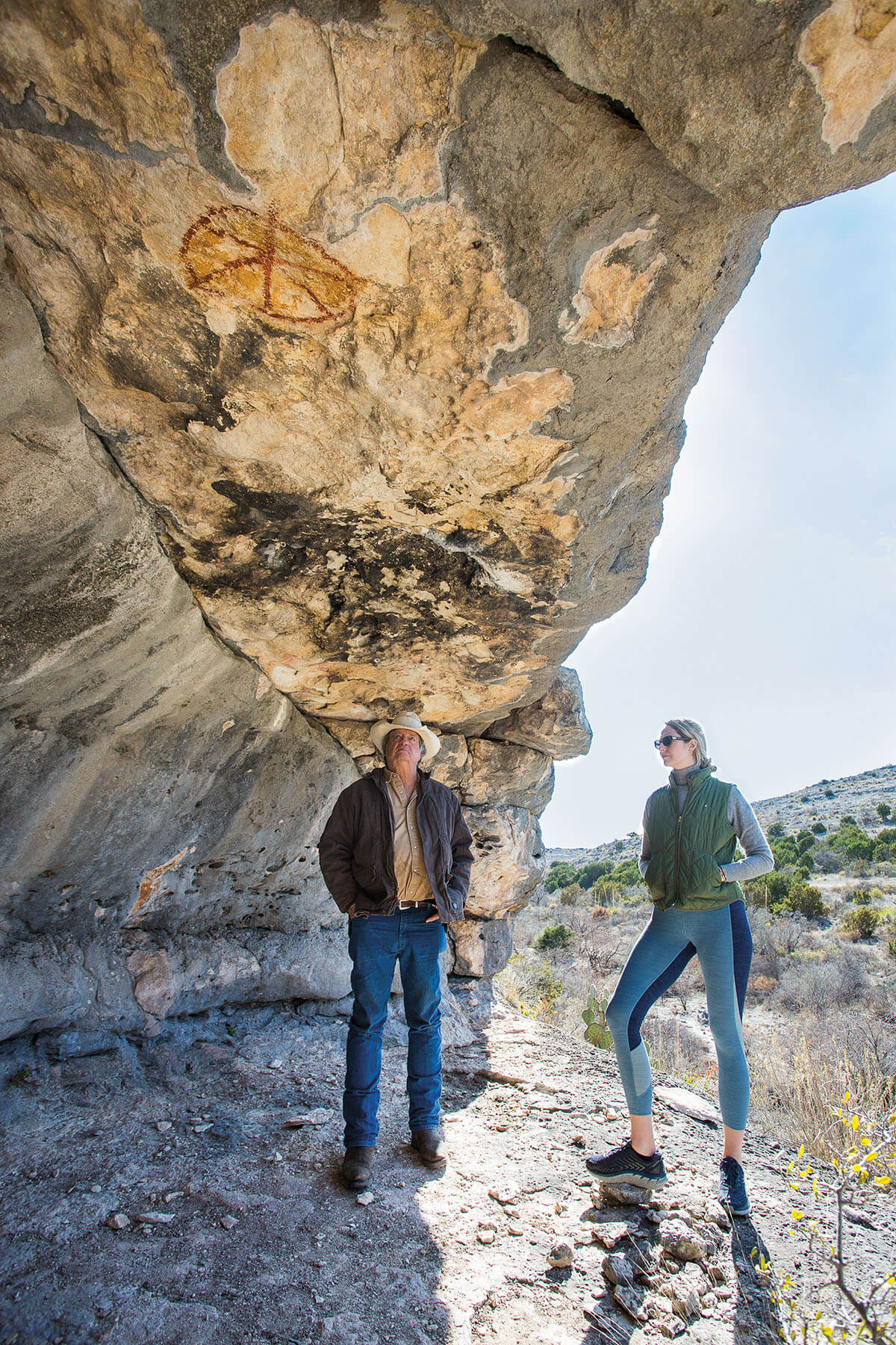 A man and woman stand inside a rock outcropping to examine cave paintings