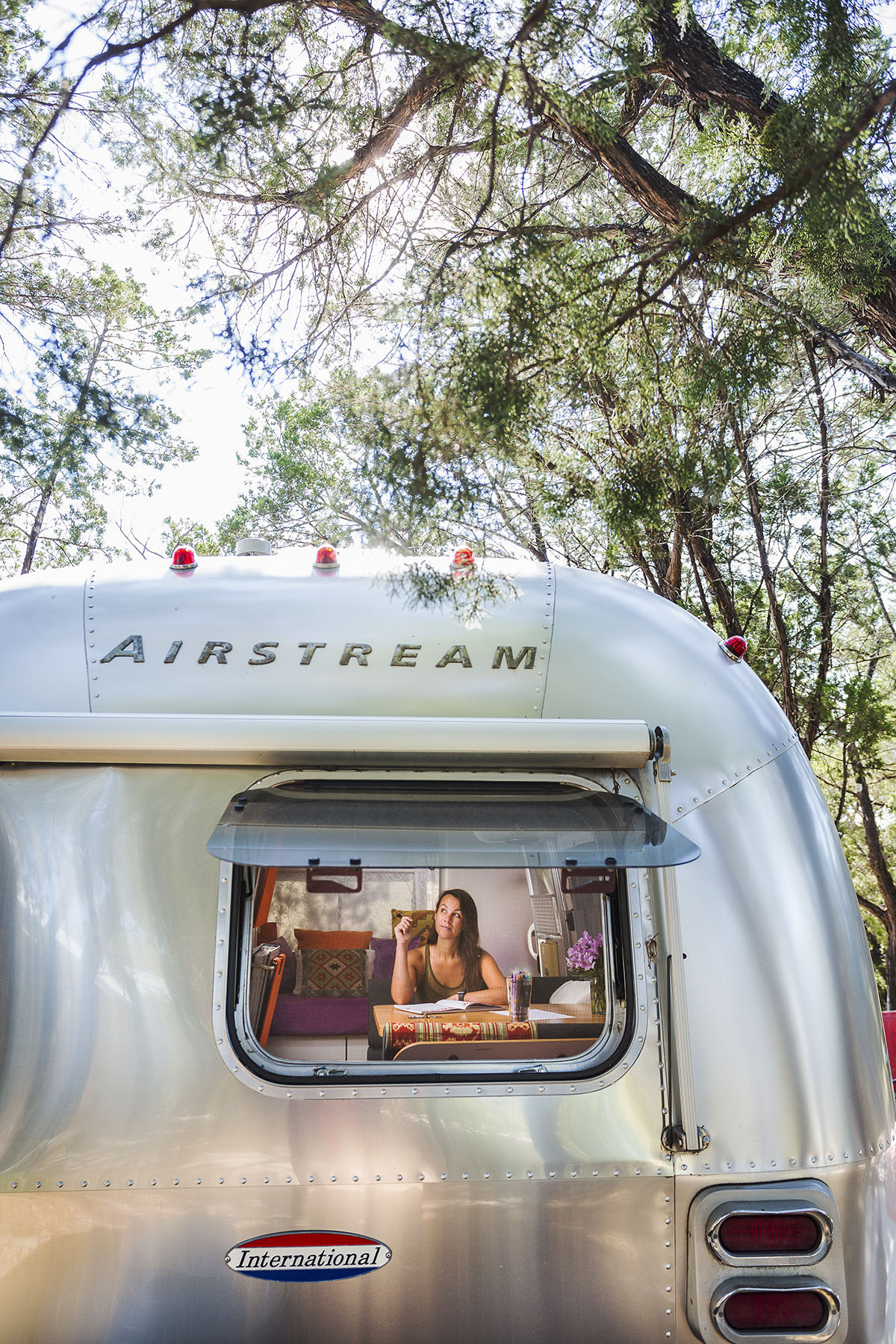 A woman looks through the window of a silver Airstream trailer