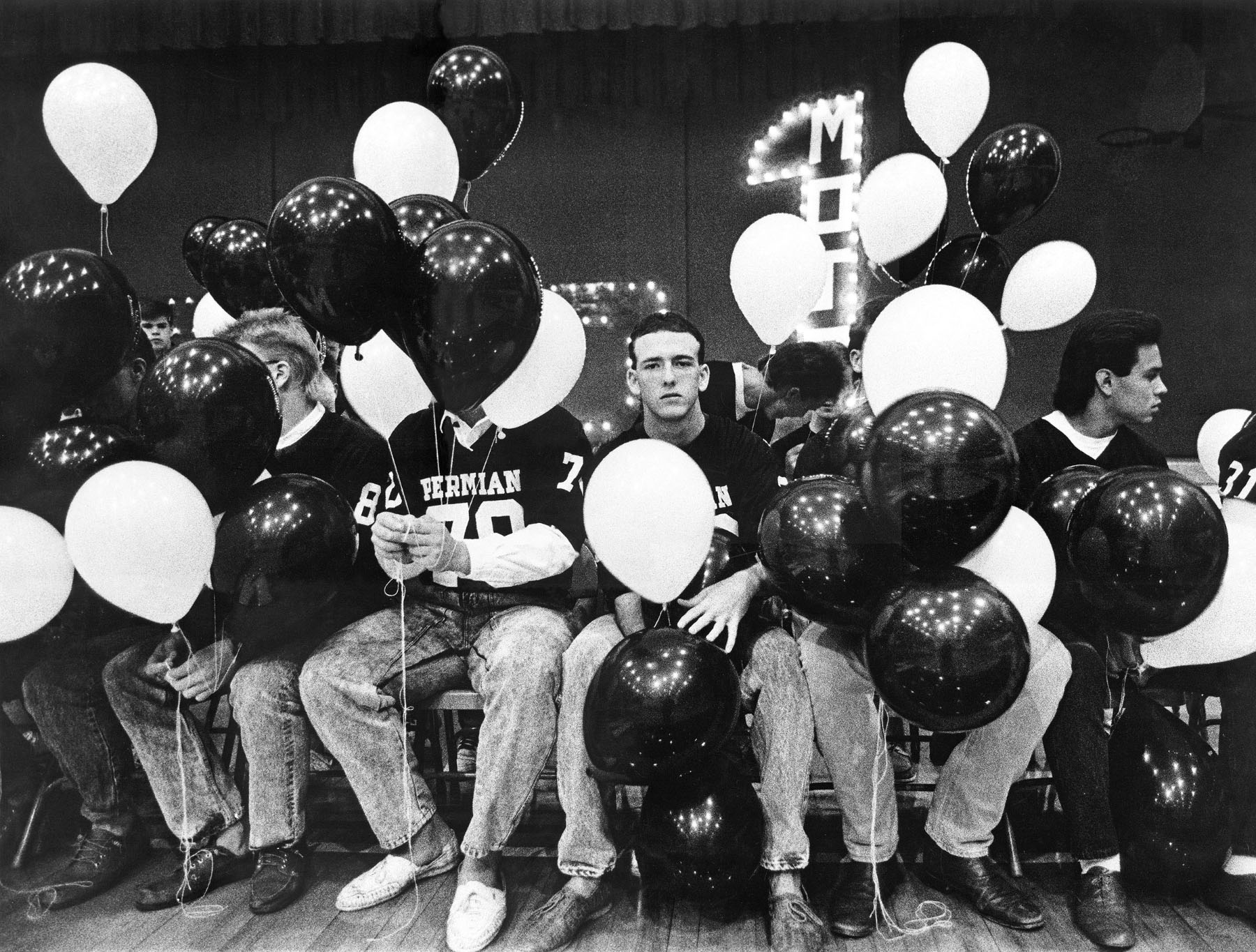 A young man looks straight-faced at the camera surrounded by black and white balloons