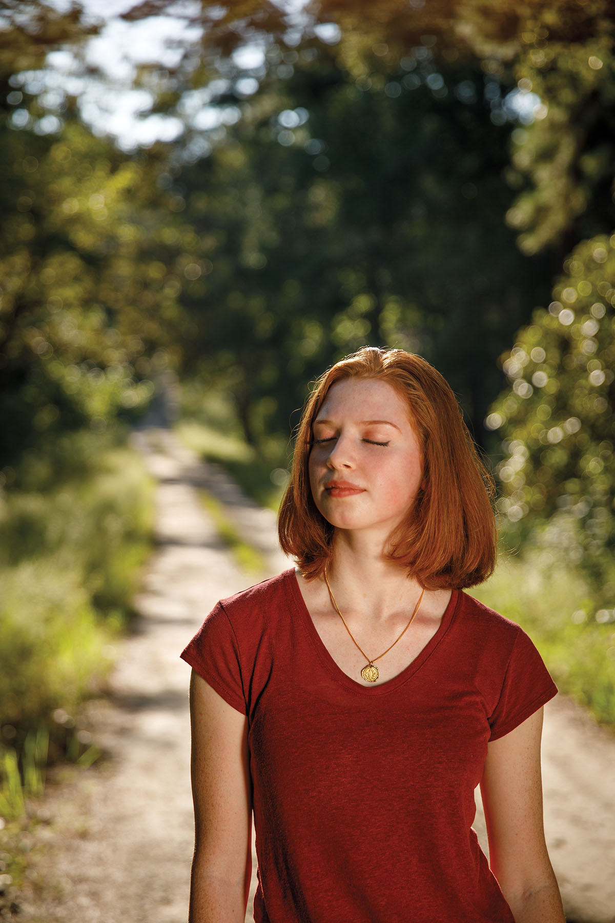 A woman stands with her eyes closed on a trail in the woods