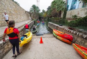 San Antonio Riverwalk tour drop their kayaks in the water at the boat ramp.